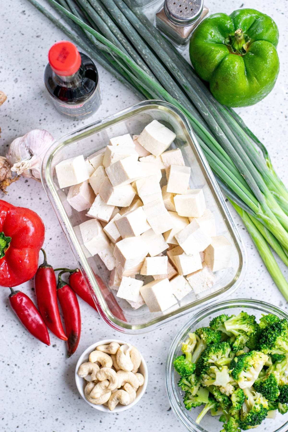 Top view of chopped tofu, fresh vegetables, cashews, and seasonings arranged on a white countertop—perfect for a Vegan Kung Pao or a Vegetarian Chinese inspired dinner.