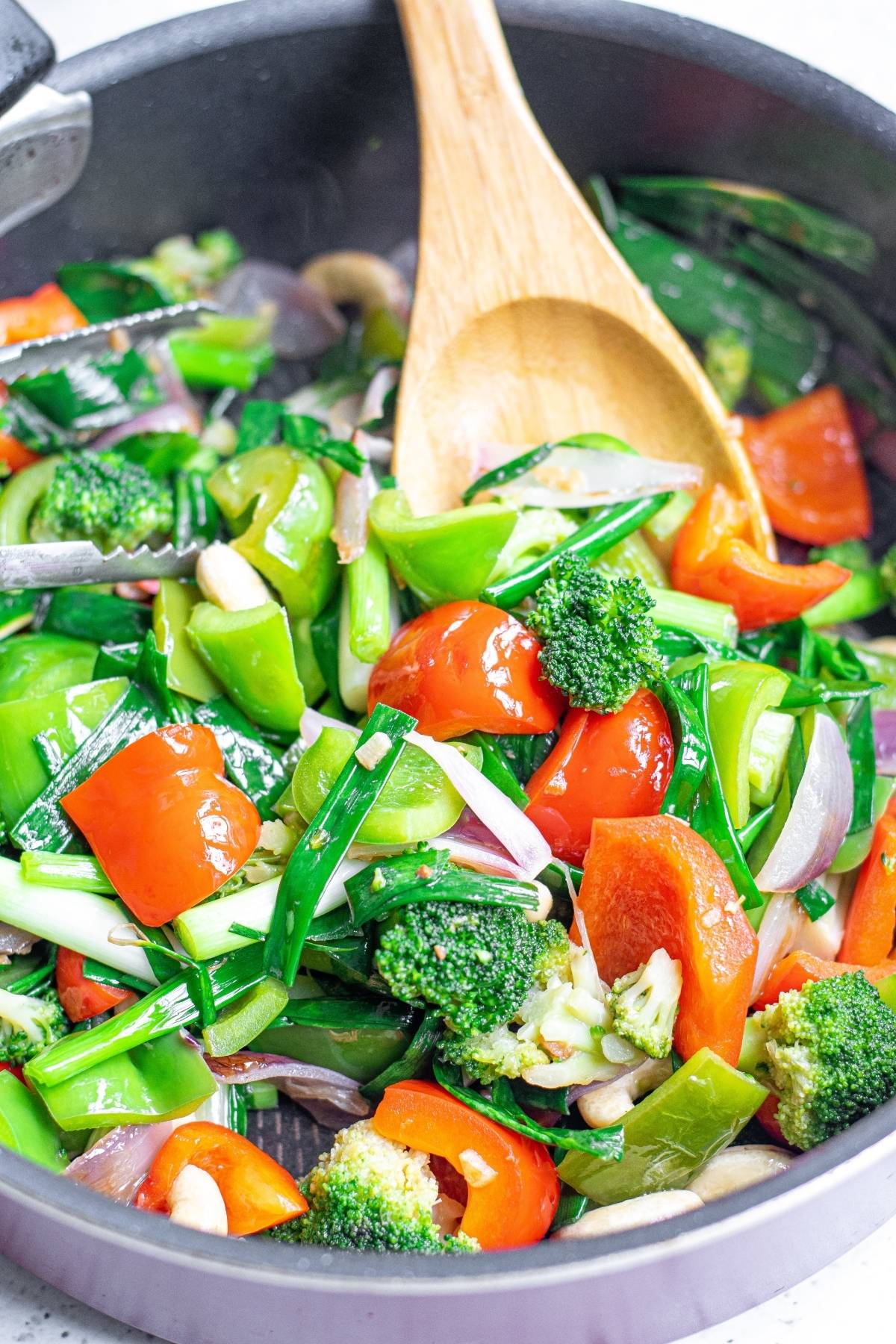 Colorful stir-fried vegetables, including broccoli and bell peppers, sizzle in a pan with a wooden spoon—perfect for making Vegan Kung Pao.