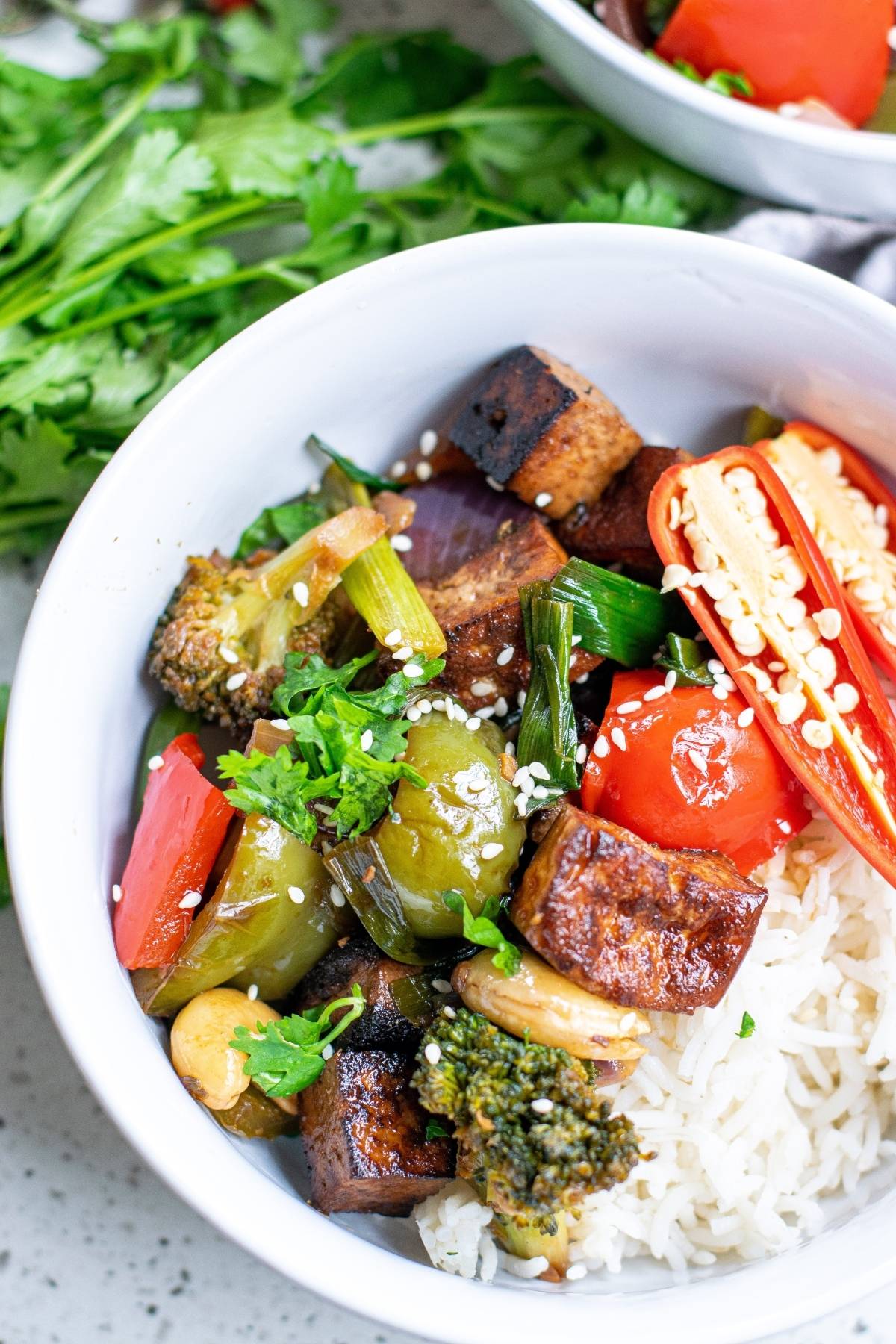 A bowl of rice topped with tofu, broccoli, peppers, tomatoes, scallions, and sesame seeds—a perfect Vegetarian Chinese inspired dinner.