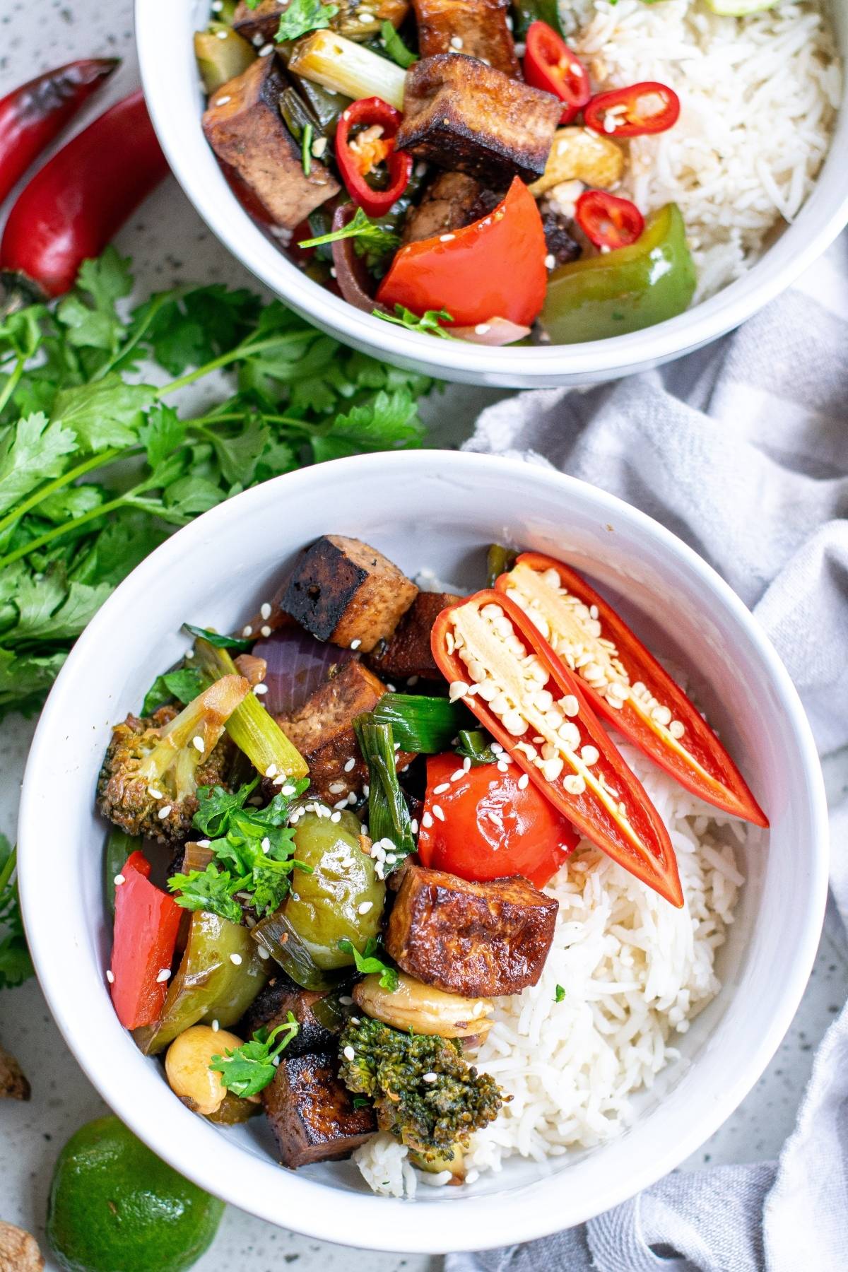 Two bowls of rice with Kung Pao Tofu, broccoli, peppers, and fresh chili slices, garnished with cilantro and sesame seeds—a vibrant Chinese food tofu recipe.
