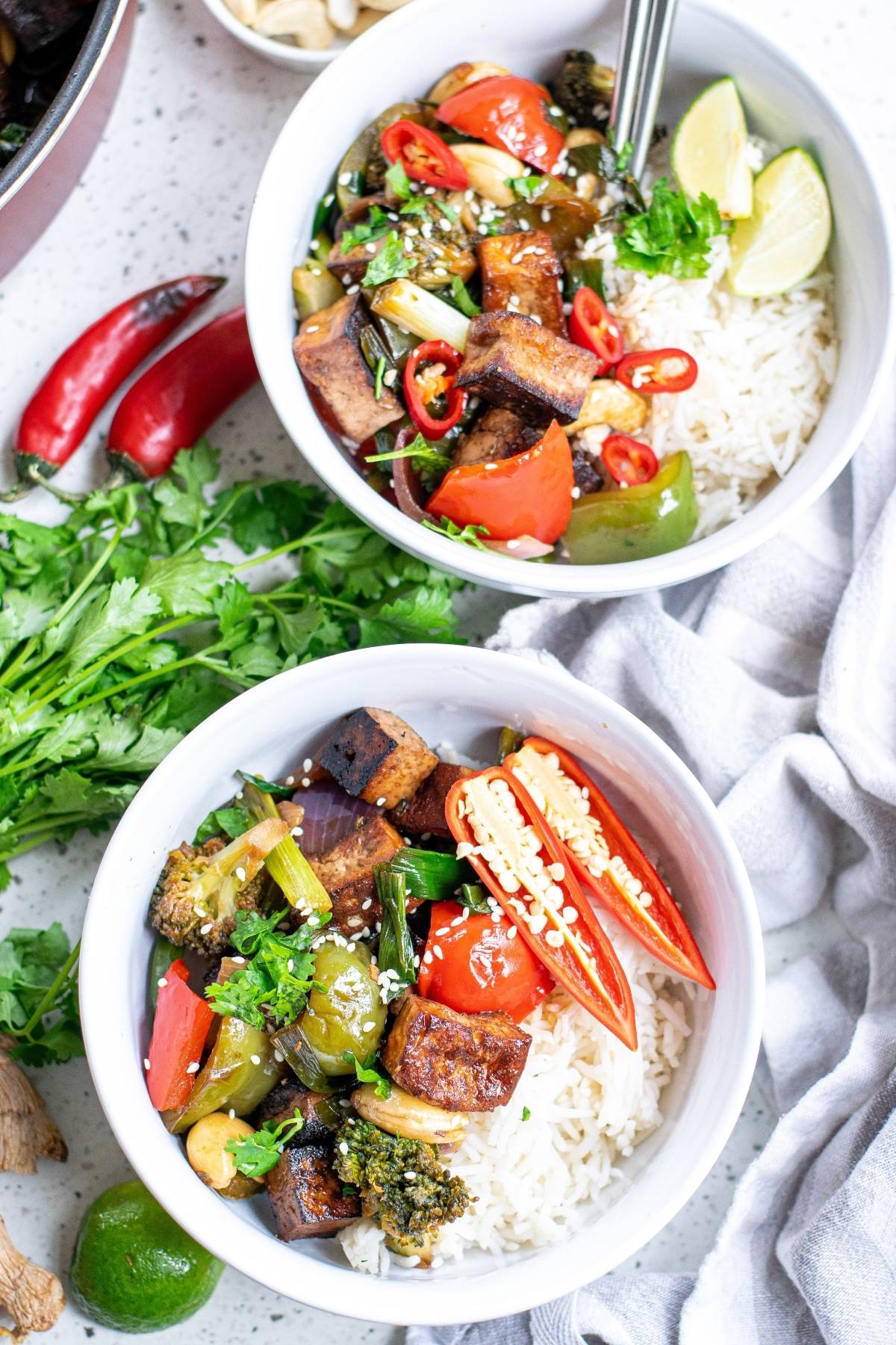 Two bowls of rice with Kung Pao Tofu, stir-fried vegetables, red chili, lime wedges, and fresh cilantro—an irresistible Vegetarian Chinese inspired dinner perfect for any vegan dinner recipe collection.