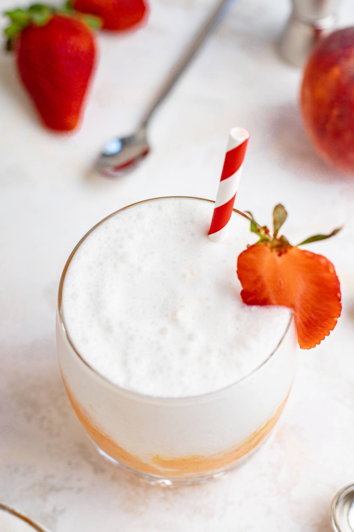 A foamy peach and strawberry drink with a red-striped straw and sliced strawberry garnish, inspired by a frozen mango cocktail.