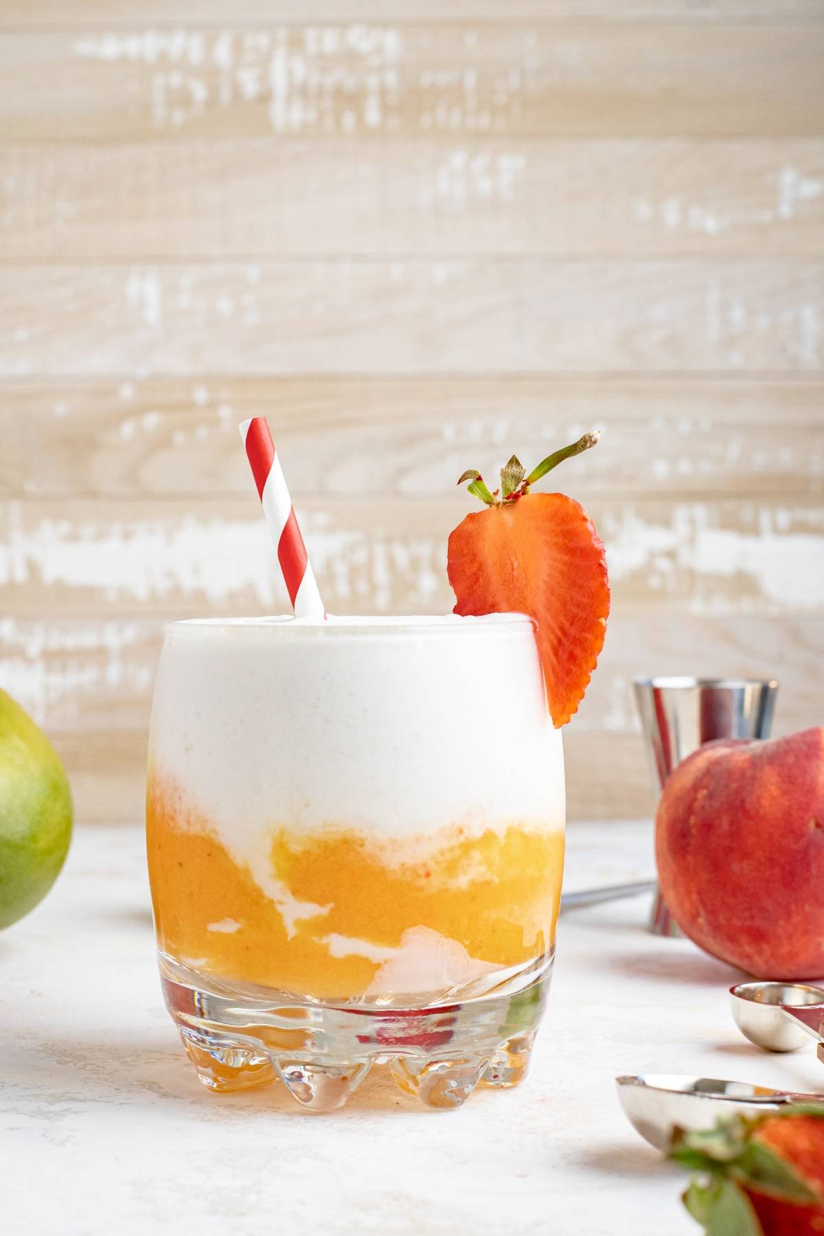 A layered slushie drink recipe featuring orange and white swirls, topped with a strawberry slice and a red striped straw, perfect for summer refreshment.
