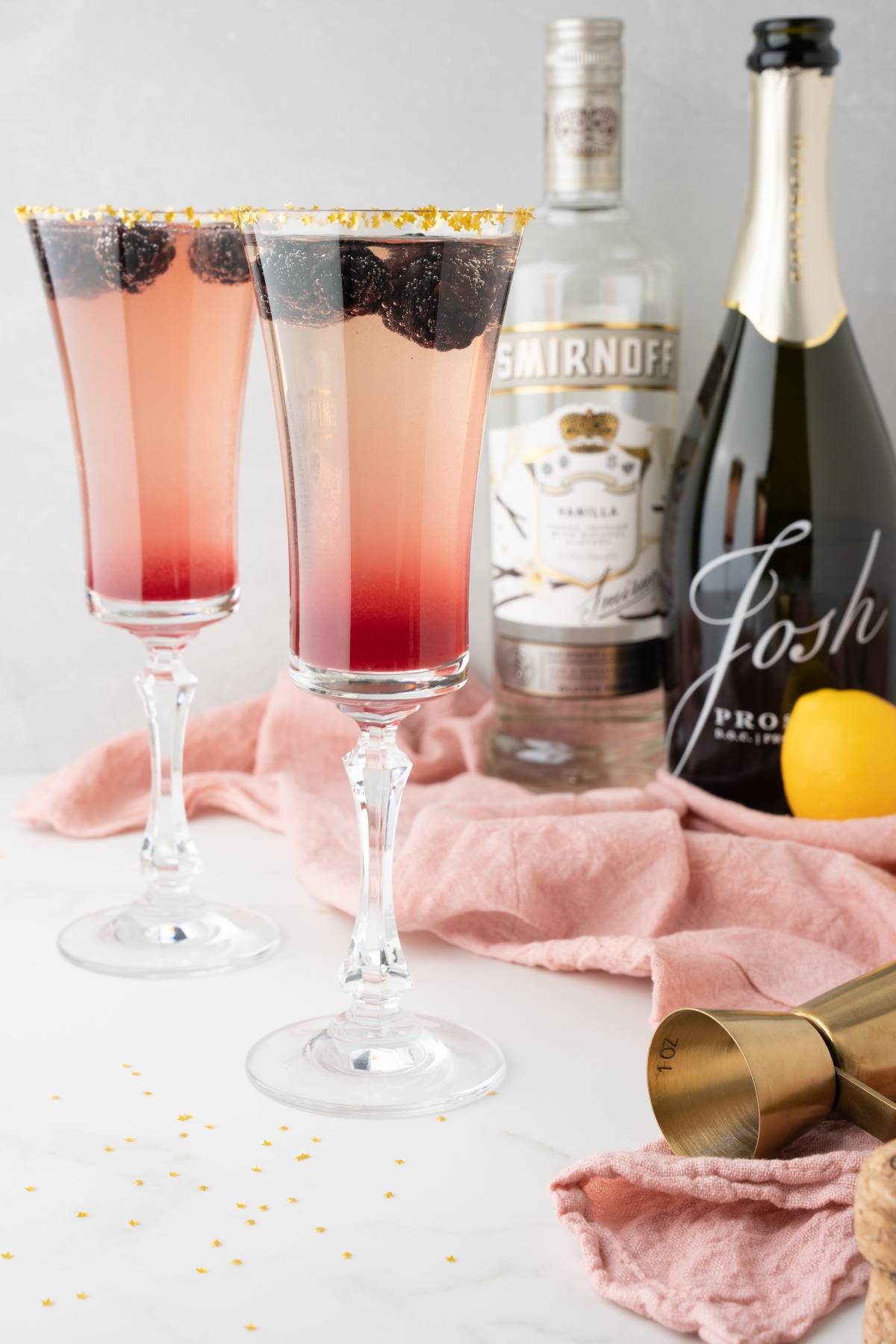 Two berry cocktails in flutes with Smirnoff vodka, Josh Prosecco, lemon, and gold sprinkles—a sparkling Lemon Berry Prosecco Cocktail perfect for your next Christmas or New Year’s Eve celebration.