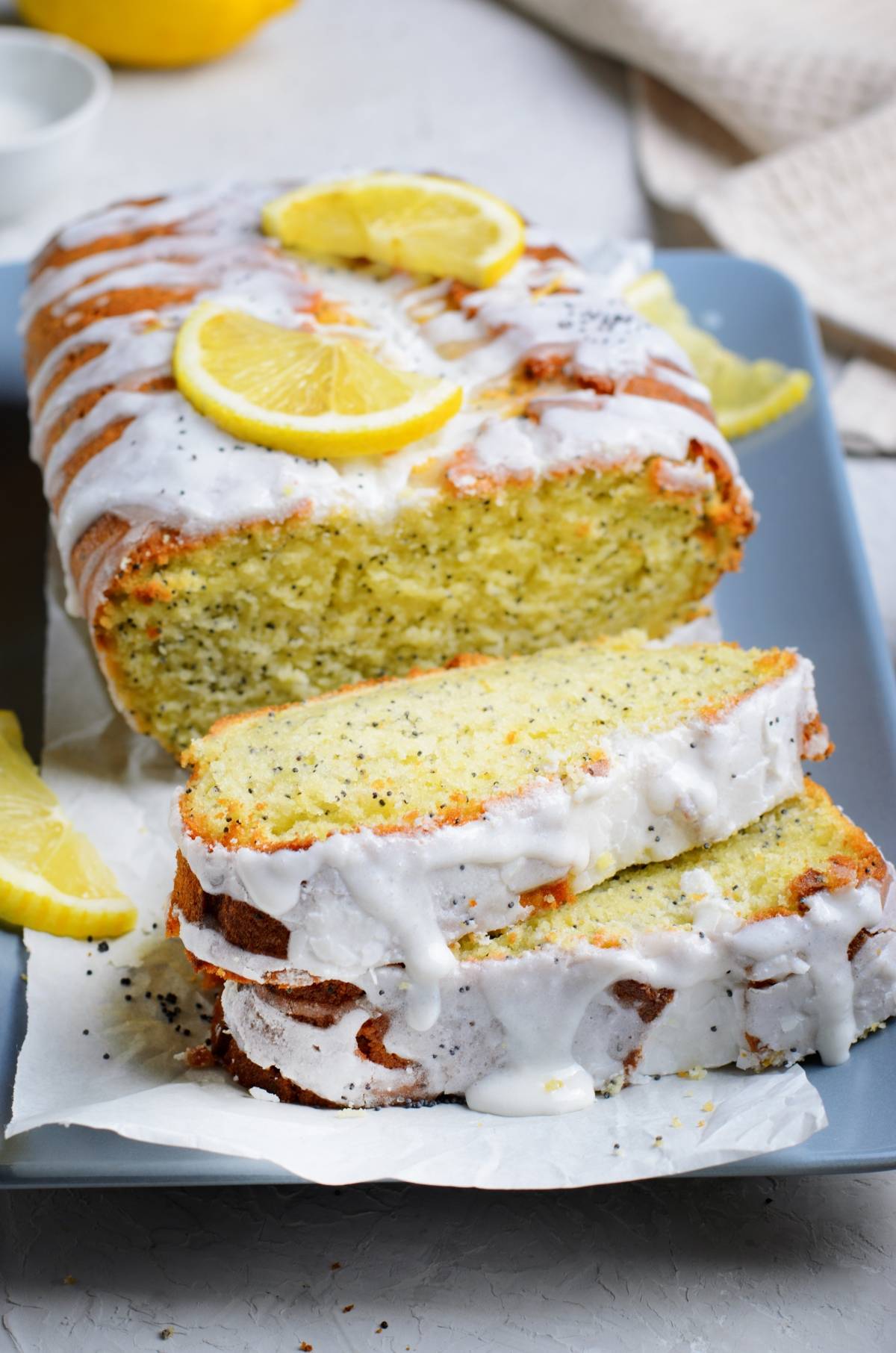 Lemon poppy seed loaf with icing, sliced and garnished with lemon wedges on a tray—a classic lemon poppy seed loaf perfect for any occasion.