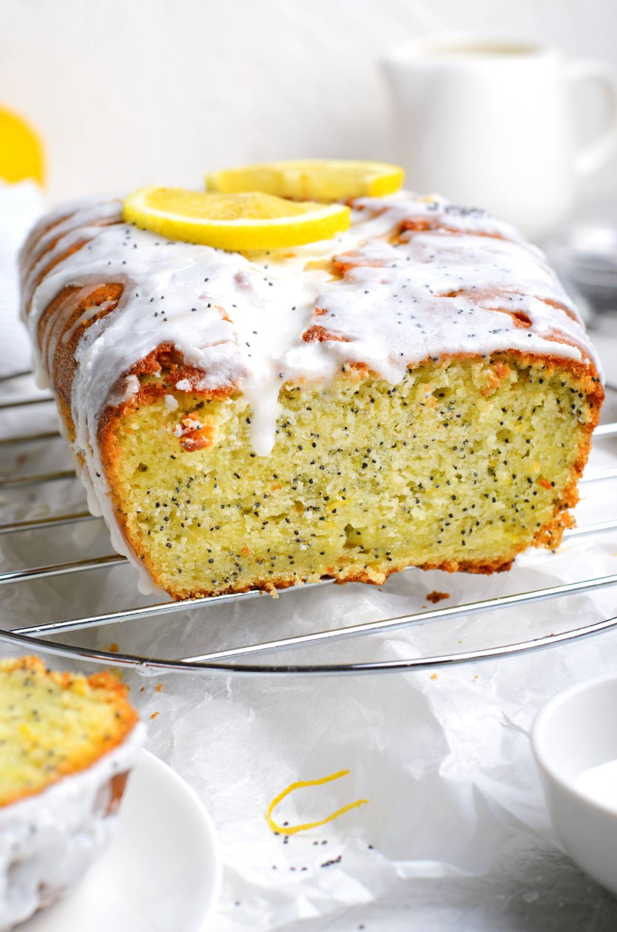 Lemon poppy seed loaf with a drizzle of white icing and fresh lemon slices on top, cooling on a rack.