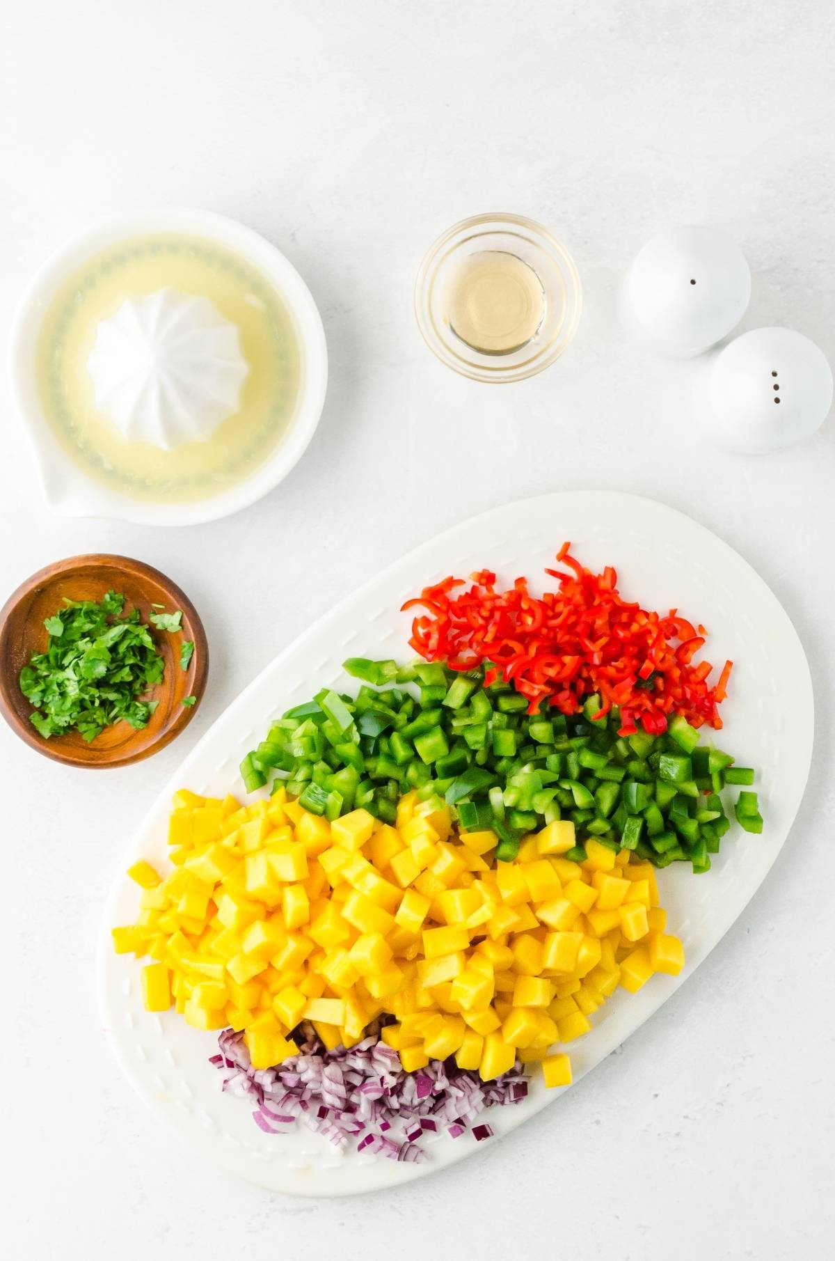 Chopped mango, red onion, green and red bell peppers on a platter with cilantro, lime juice, and salt nearby—perfect for a vibrant summer salsa recipe.