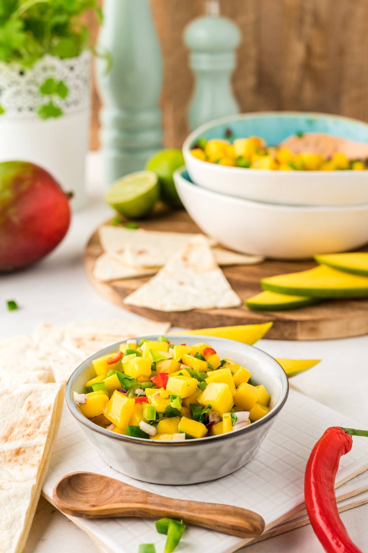 A small bowl of fresh Mexican fruit salsa with chopped vegetables, tortilla chips, and sliced mango nearby.