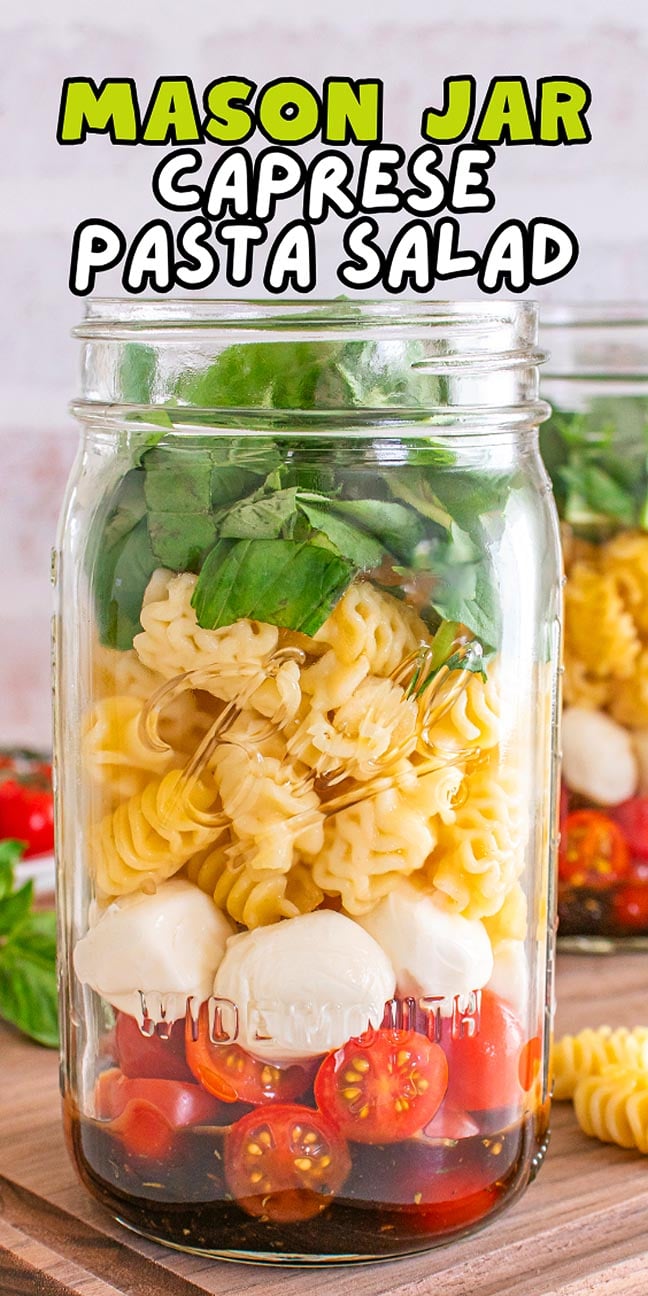 A mason jar Caprese pasta salad filled with cherry tomatoes, mozzarella, pasta, basil, and spinach—fresh flavors layered for a perfect meal on the go.