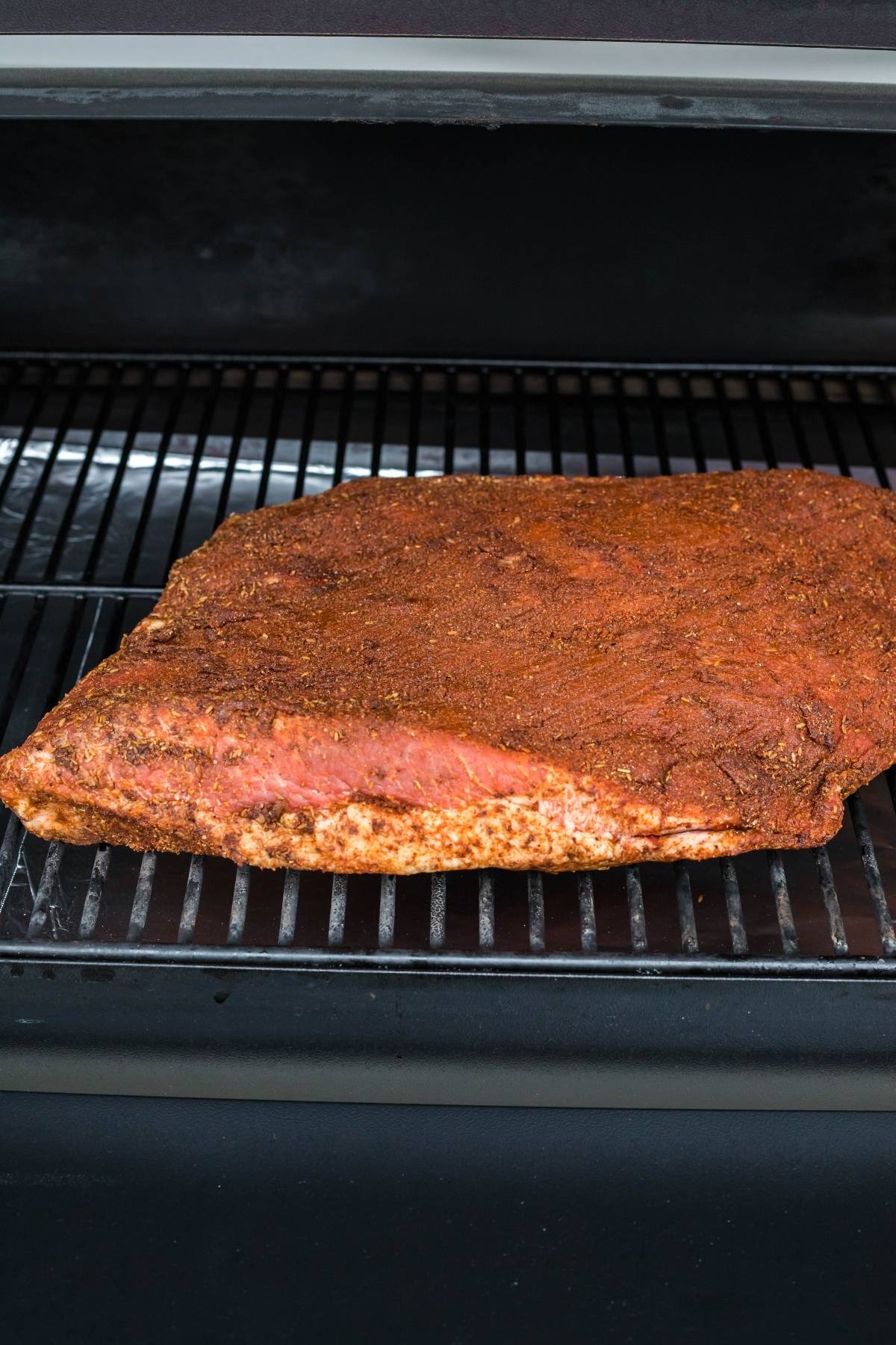 Seasoned brisket on a grill rack, ready to become flavorful mesquite smoked brisket, with a dark background.