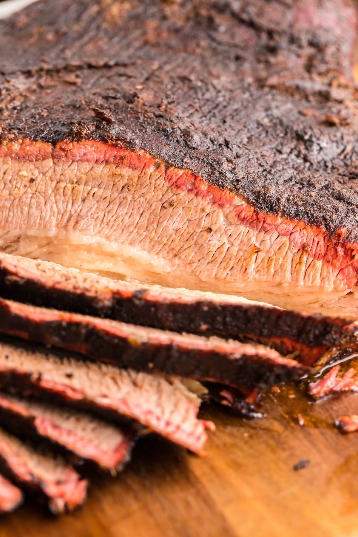 Sliced smoked brisket made in a Traeger grill, showing a pink smoke ring and juicy, tender meat on a wooden board.