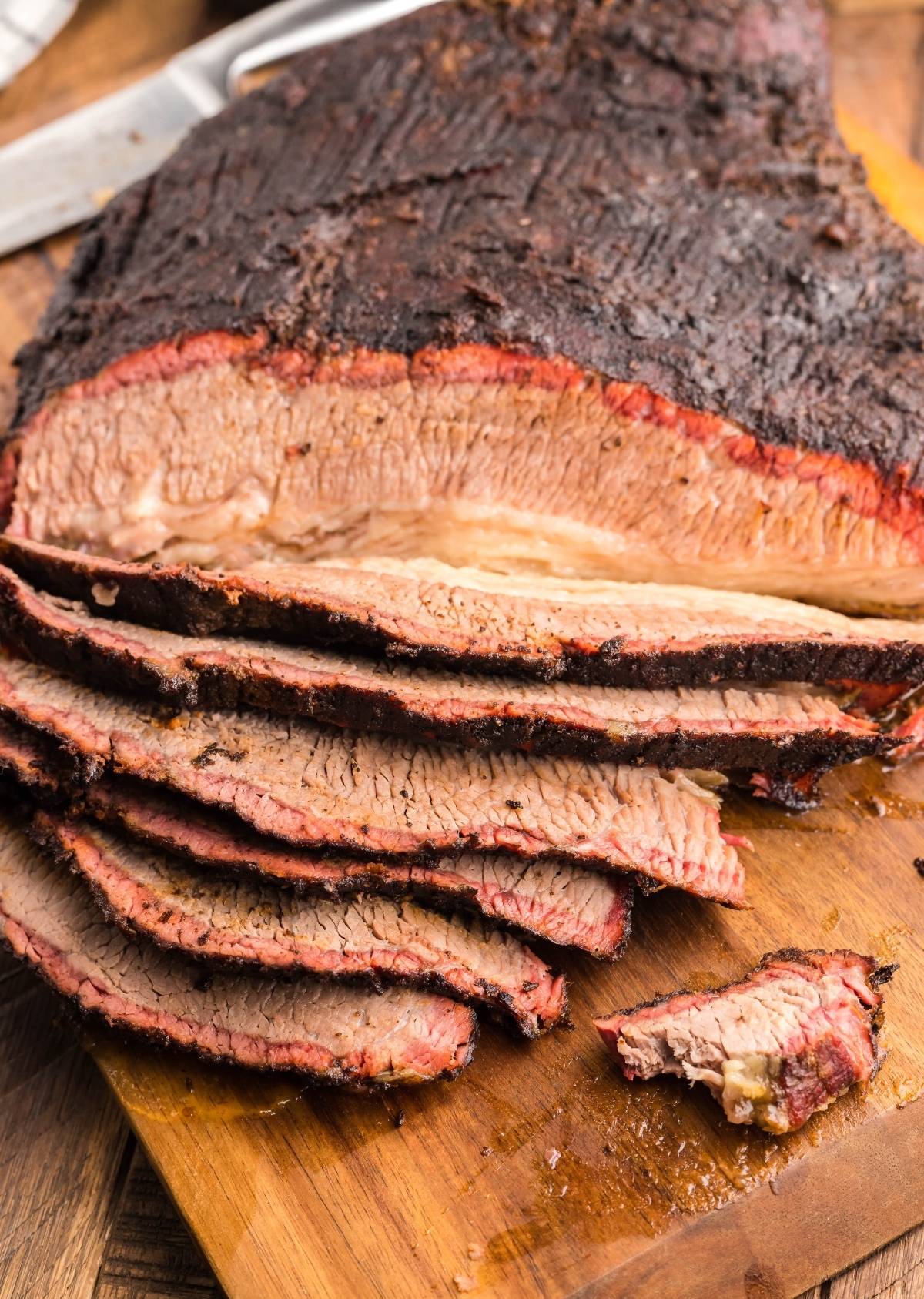 Sliced mesquite smoked brisket on a wooden cutting board, showing juicy, tender texture and a dark, seasoned crust from a flavorful dry rub for brisket.