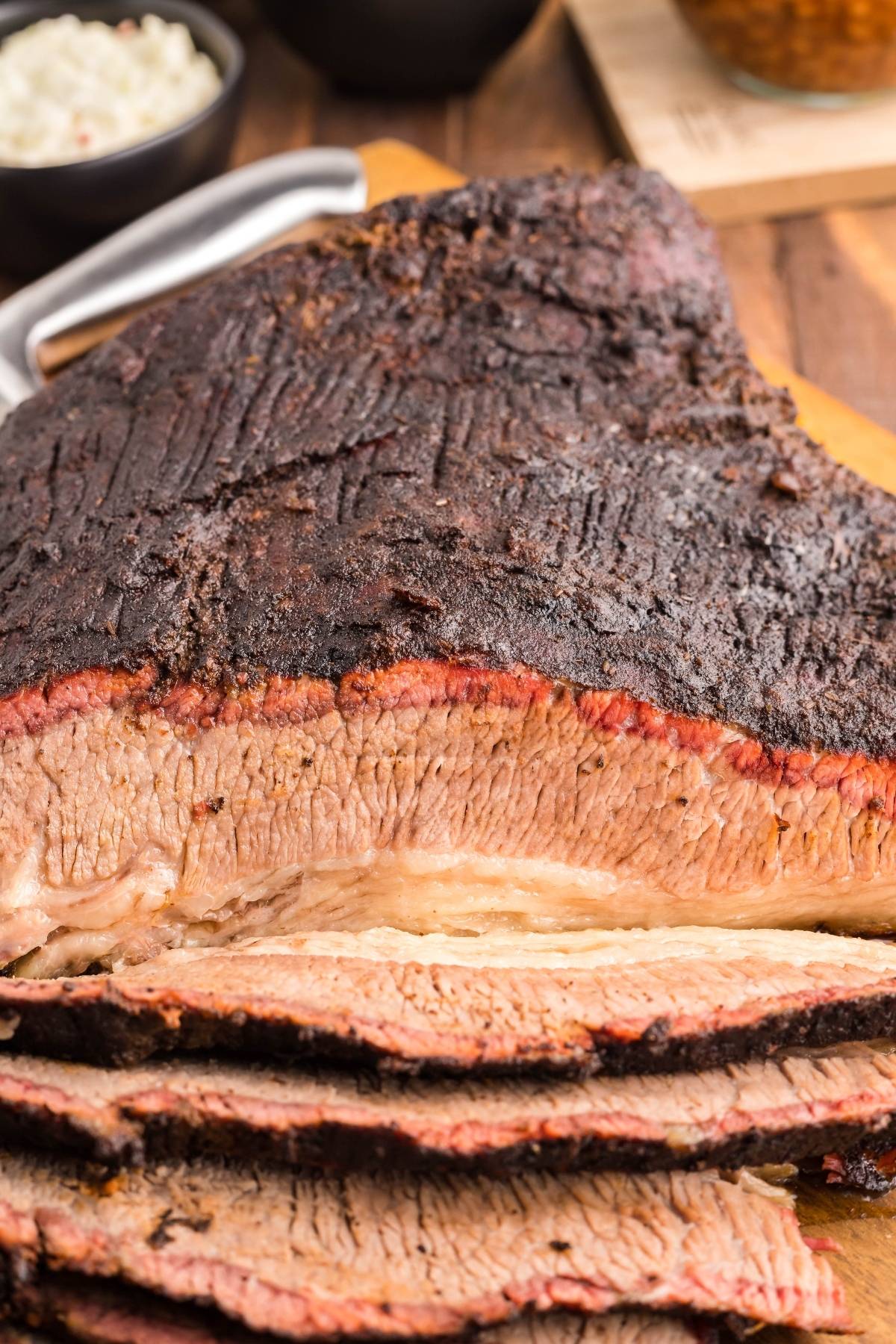 Sliced mesquite smoked brisket on a cutting board with a dark, seasoned crust and visible smoke ring, made in a Traeger grill for bold flavor.