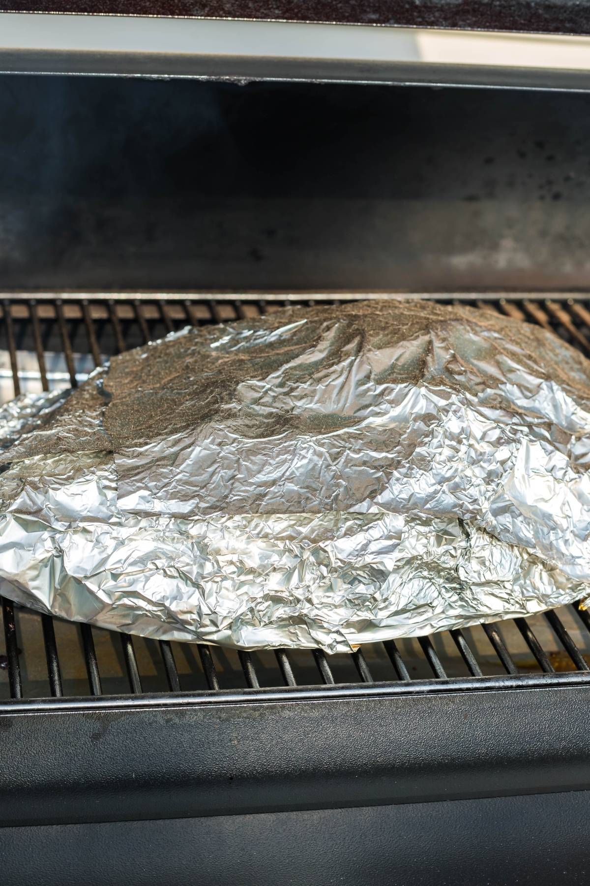 A large piece of meat coated with a dry rub for brisket and wrapped in foil, cooking slowly on a grill or smoker.