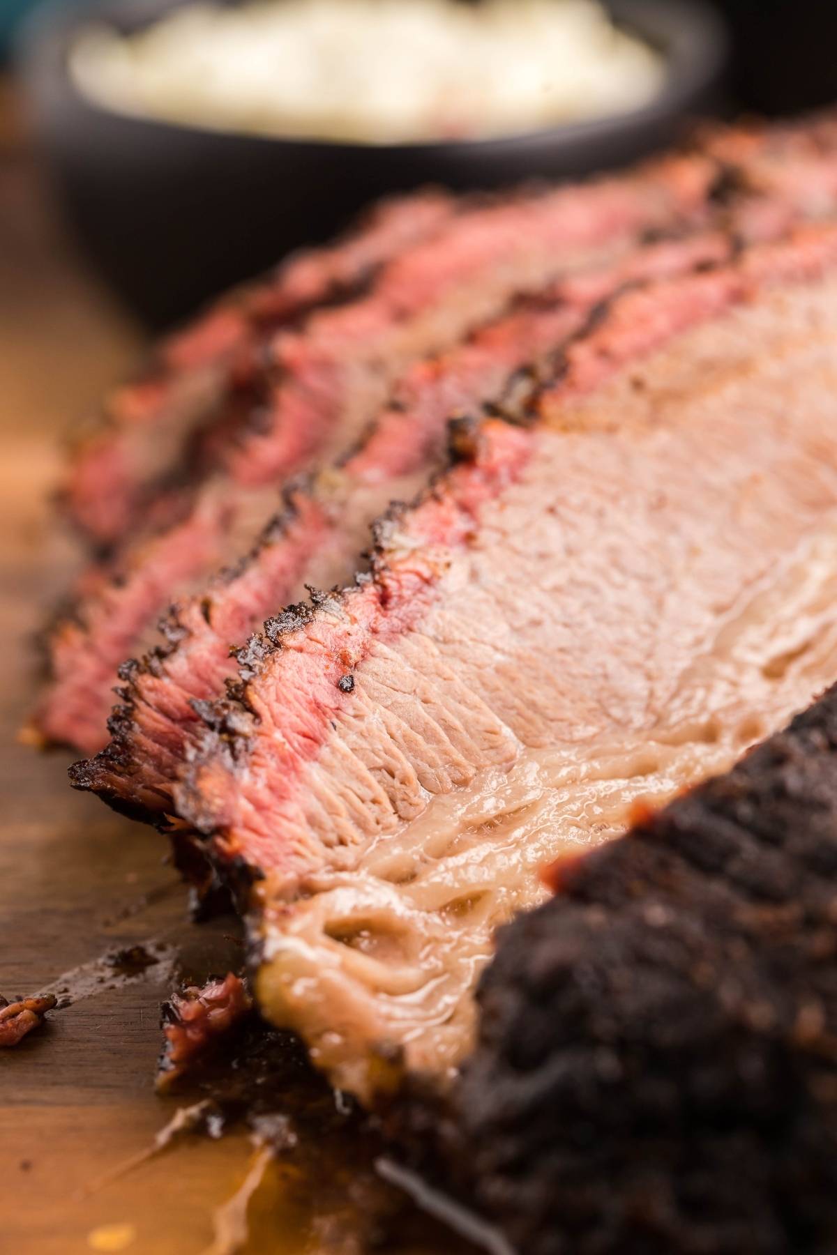 Close-up of sliced smoked brisket with a dark crust and juicy pink interior on a wooden board—an irresistible look at this easy Texas smoked brisket recipe, perfect for those wanting to know how to make smoked brisket at home.