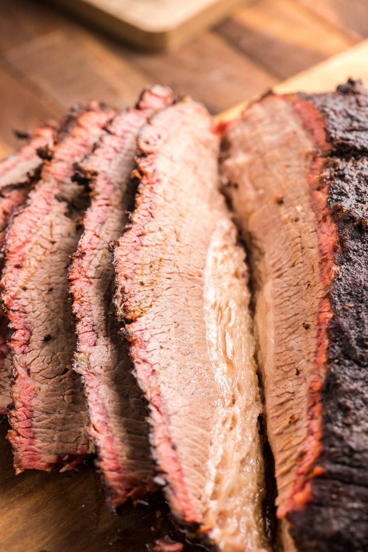 Sliced smoked brisket with a juicy center and a dark, seasoned crust from an easy Texas smoked brisket recipe, served on a wooden surface.