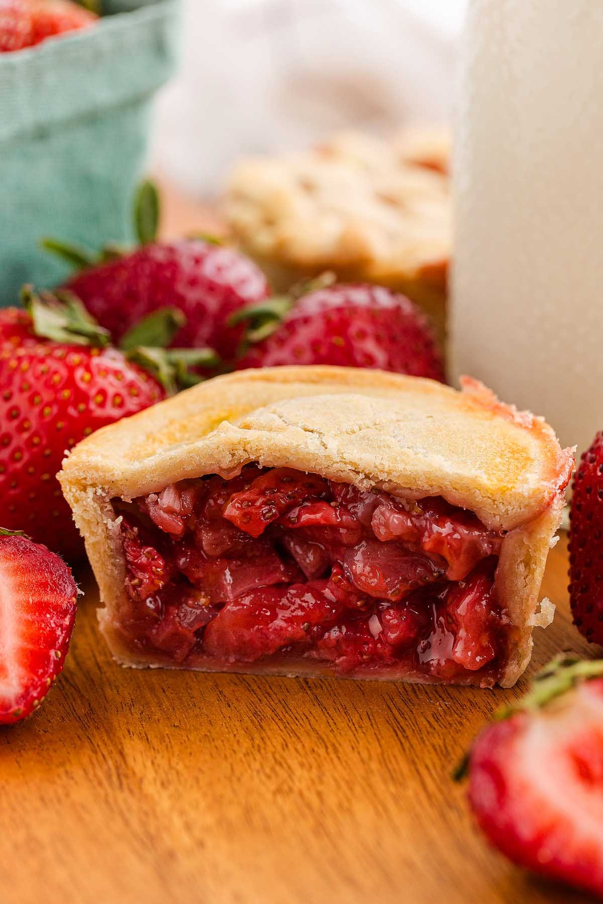 A mini strawberry pie with a flaky crust and juicy filling, surrounded by fresh strawberries on a wooden surface—perfect for lovers of mini strawberry pies.