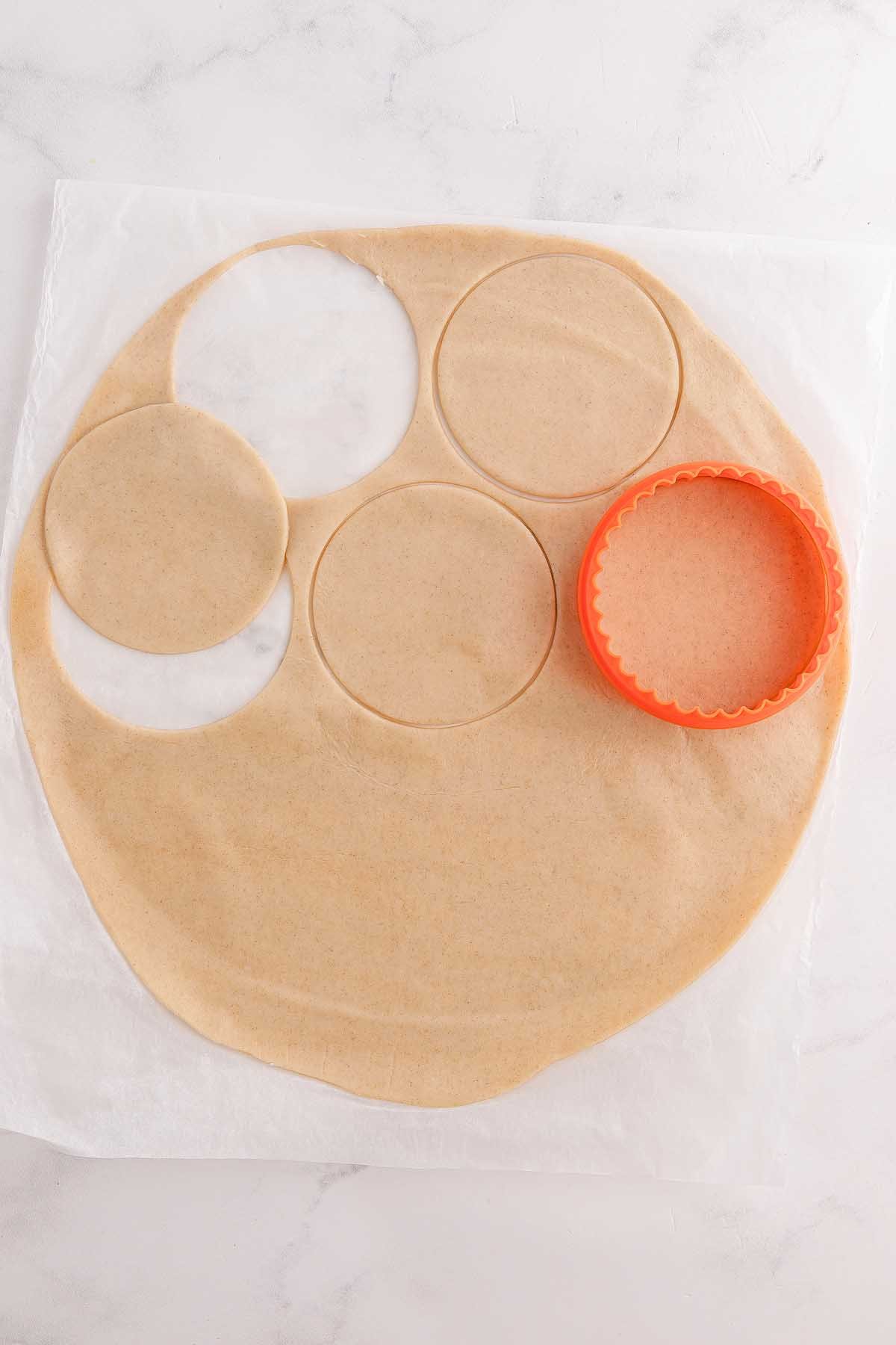 Rolled dough with three circular cutouts for mini strawberry pies and an orange cookie cutter on parchment paper.