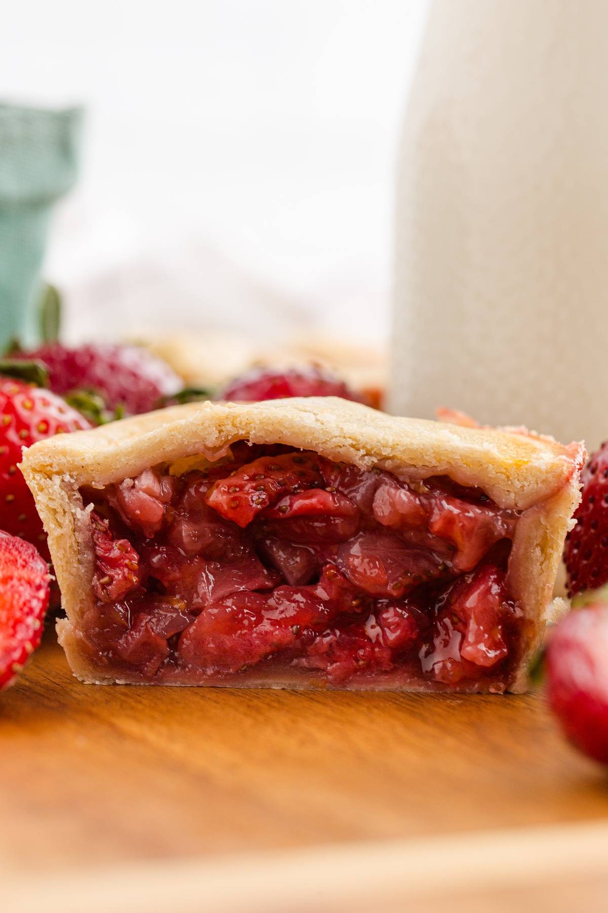 A close-up of a sliced strawberry pie showing the juicy filling and flaky crust on a wooden surface.