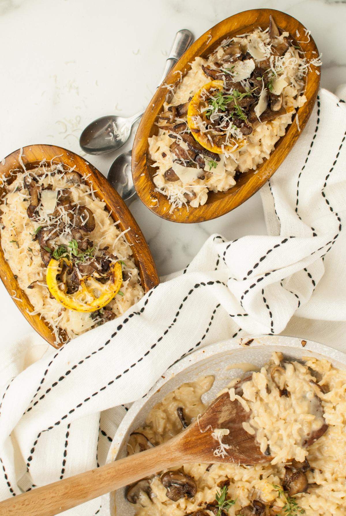 Creamy mushroom risotto in wooden bowls, topped with mushrooms and herbs, makes a perfect side dish for chicken or turkey. Served with a striped cloth and wooden spoon.