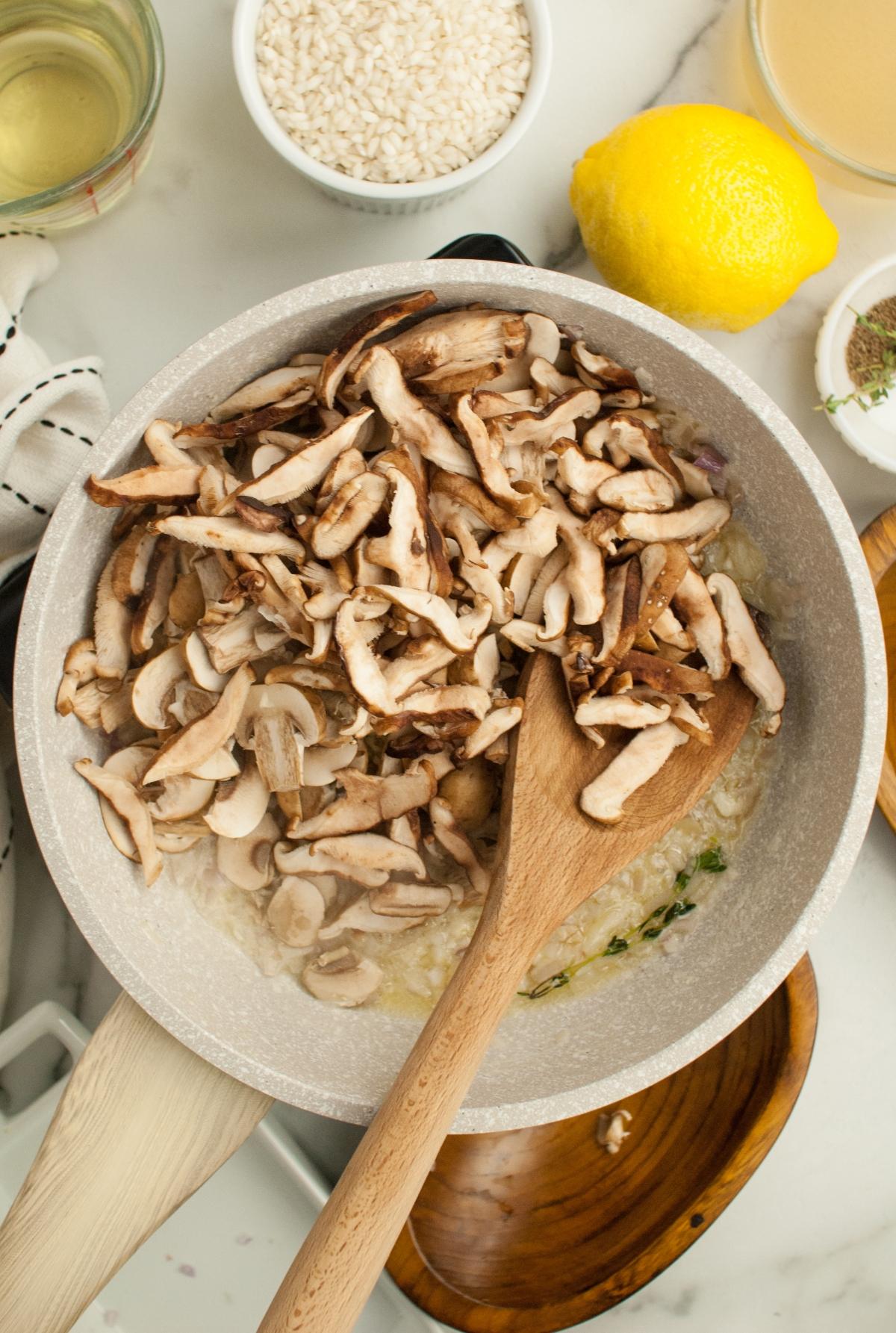 Sliced mushrooms cooking in a pan with a wooden spoon, surrounded by ingredients like lemon, rice, and a splash of white wine or Chardonnay—perfect as a side dish for chicken or turkey.