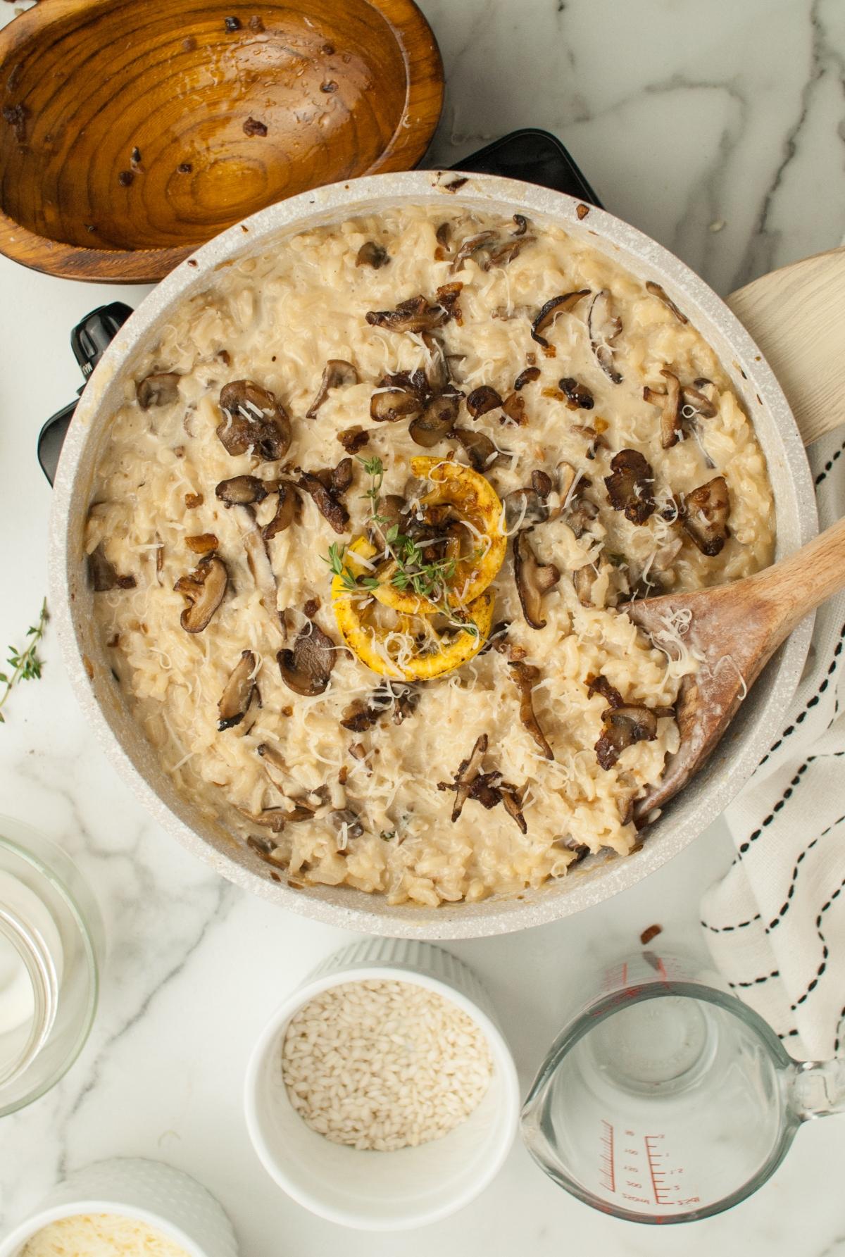 Creamy shiitake and cremini mushroom risotto in a pan, topped with herbs and lemon, with a wooden spoon and bowls nearby—an ideal side dish for chicken or turkey.