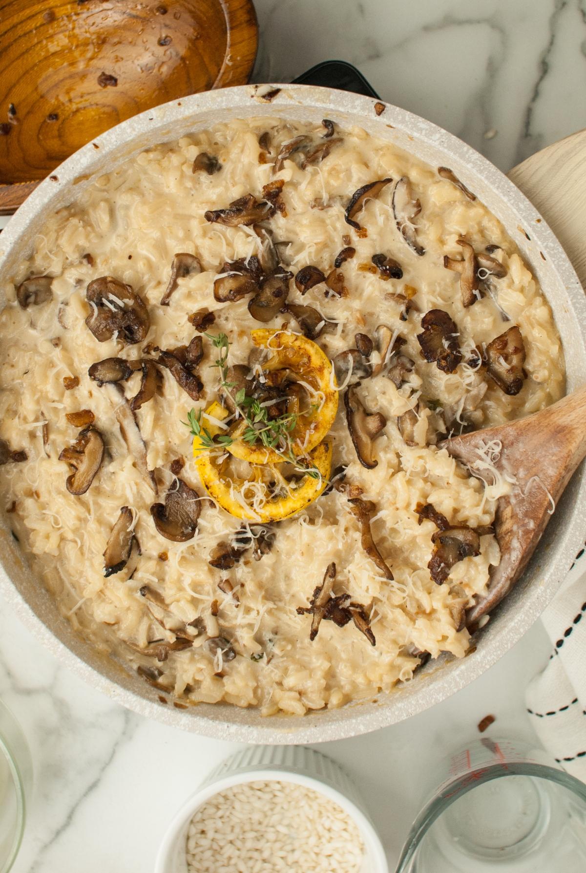 Creamy mushroom risotto in a pan, topped with sliced mushrooms, lemon, herbs, and grated cheese—perfect as a side dish for chicken or turkey.