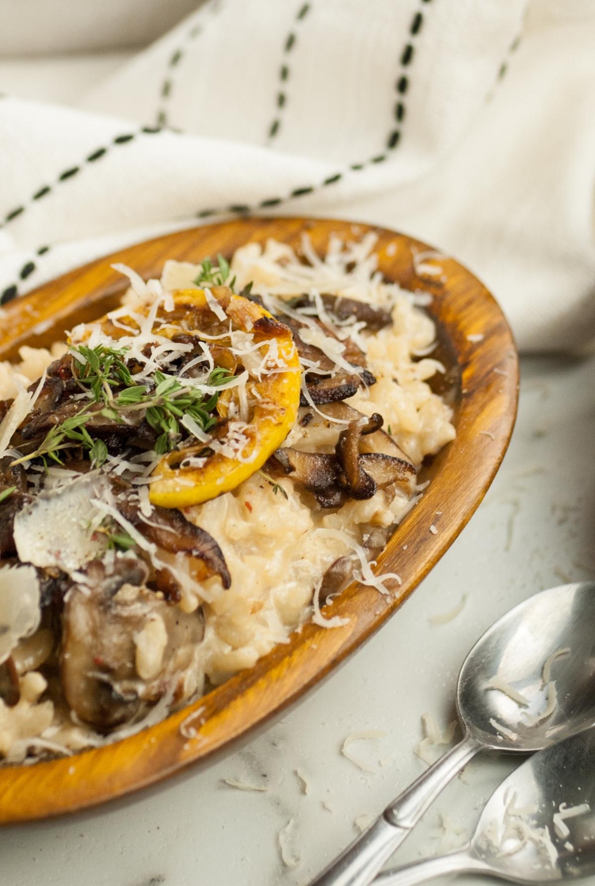 Creamy mushroom risotto with shiitake and cremini (baby bella), served in a wooden bowl, topped with herbs, lemon, and grated cheese—a perfect side dish for chicken or turkey.
