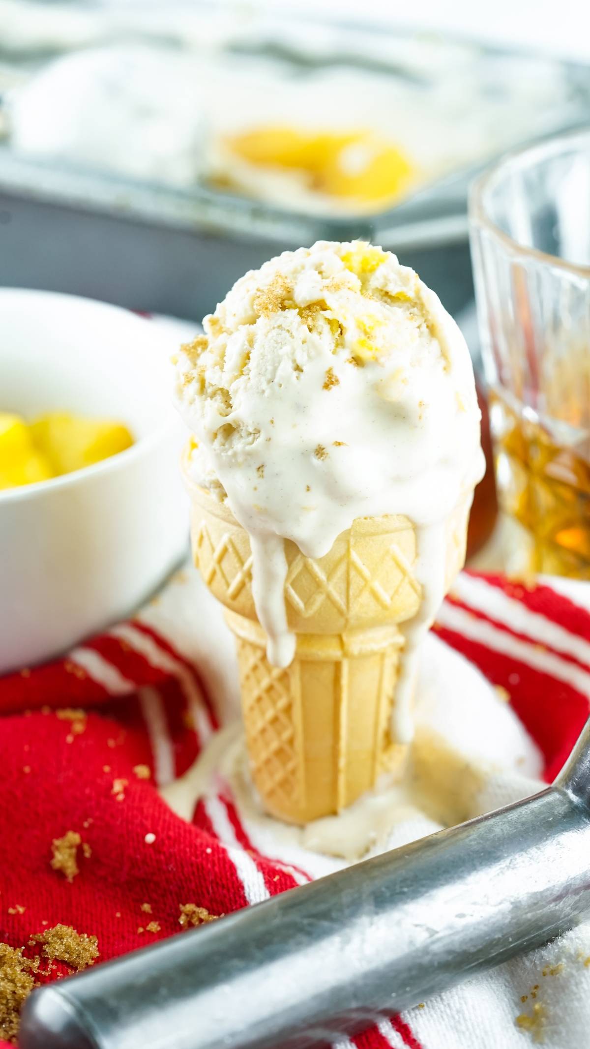 A melting no churn peach ice cream cone with crumbs on top, placed on a red striped cloth with dessert items nearby.