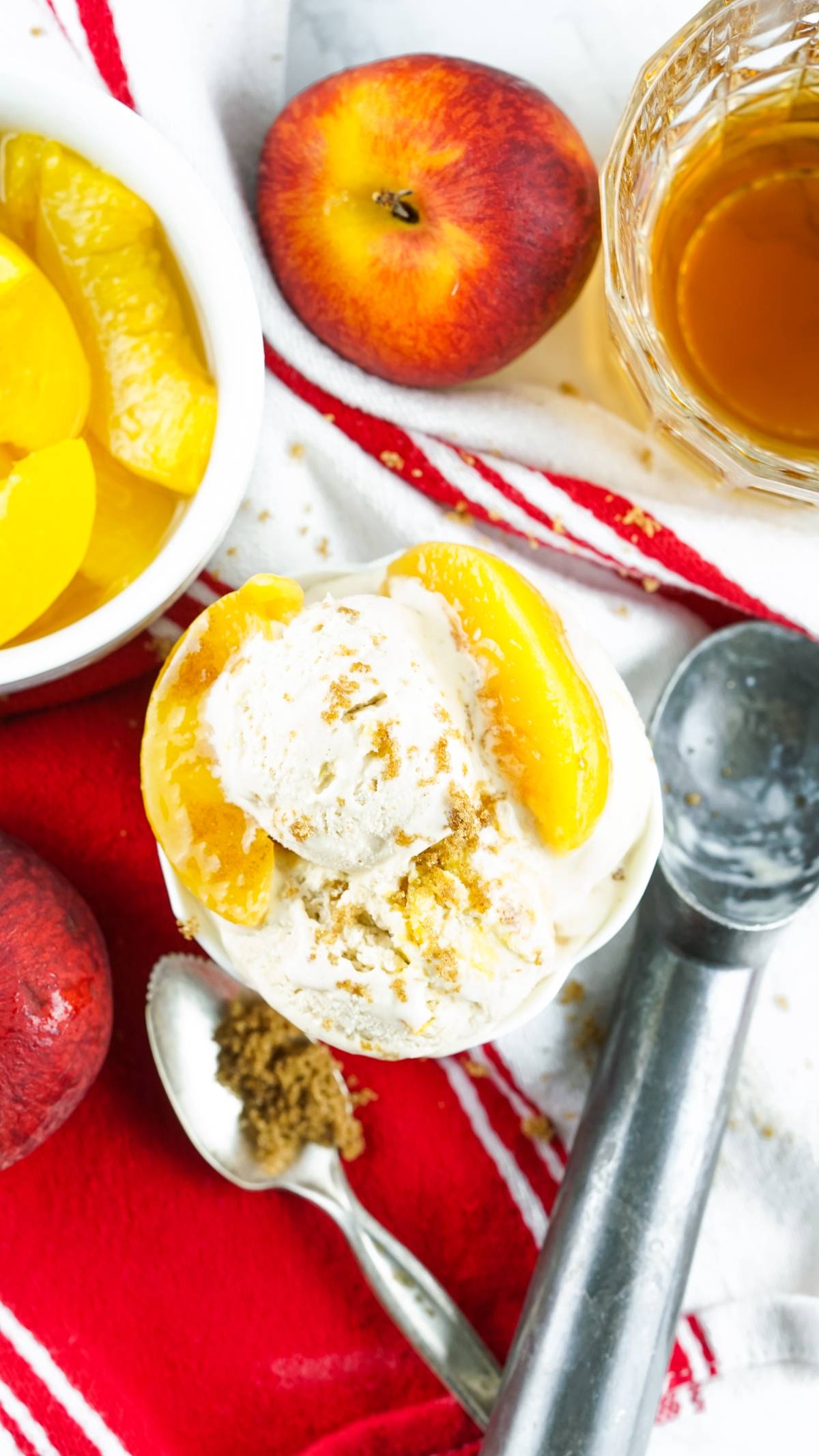 Bowl of no churn peach ice cream with fresh peach slices, brown sugar, and peaches on a red and white cloth—perfect as a boozy peach dessert.