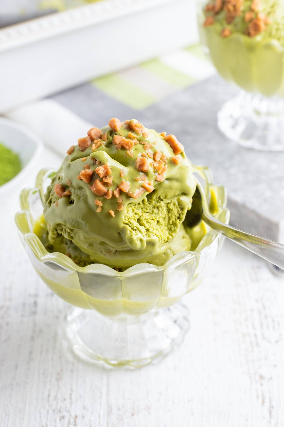 A glass dish of matcha green tea ice cream topped with chopped nuts and a spoon—try this no churn ice cream recipe for a creamy treat without an ice cream machine.