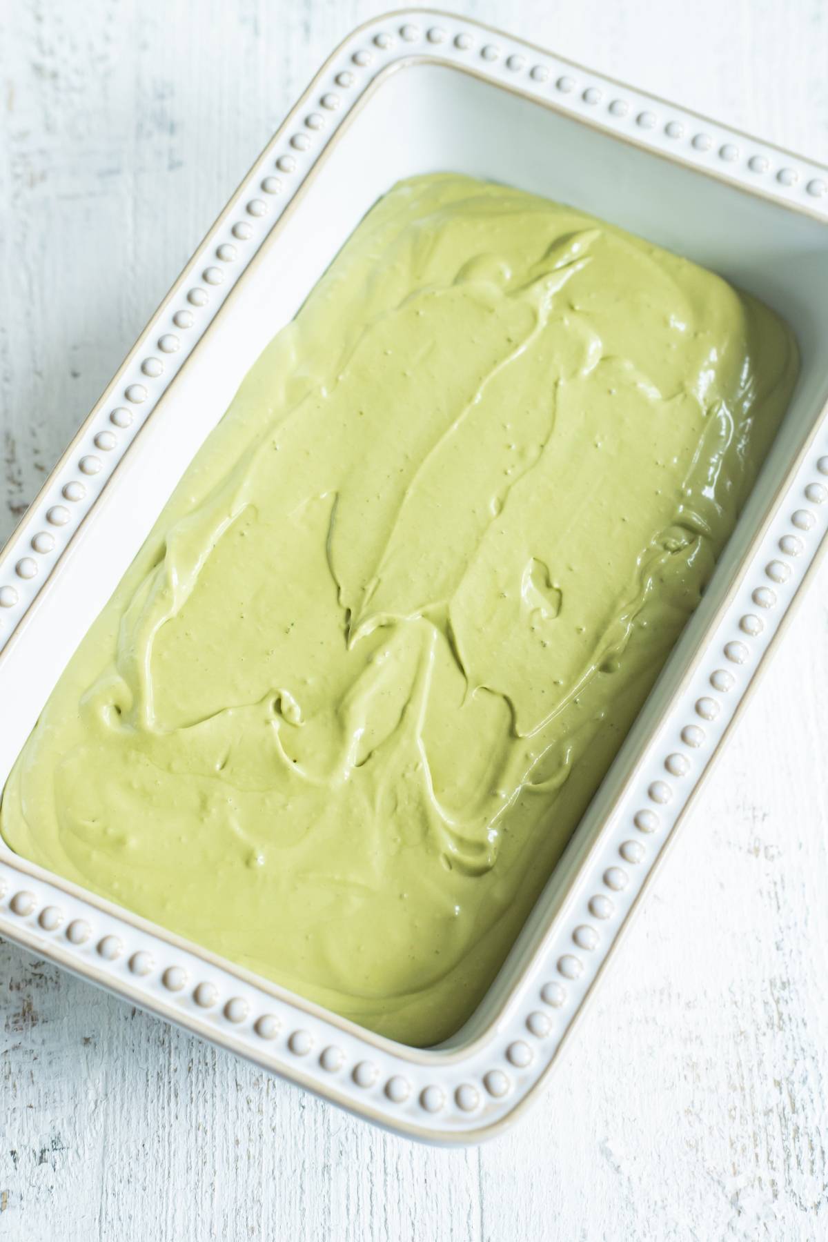 A white rectangular dish filled with smooth, light green matcha ice cream, made without a machine, sits on a white surface.