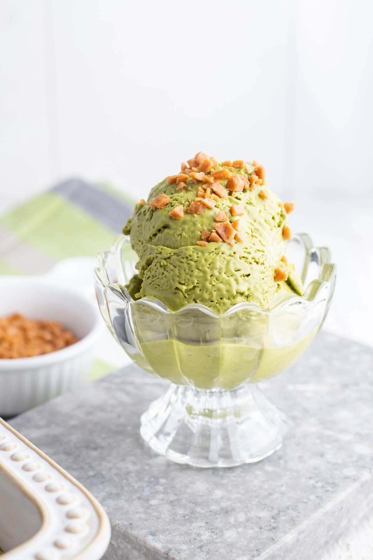 No Churn Matcha Dulce de Leche Ice Cream in a glass bowl, topped with chopped nuts, sits on a gray surface with a blurred background—a delightful recipe using Dulce de Leche.