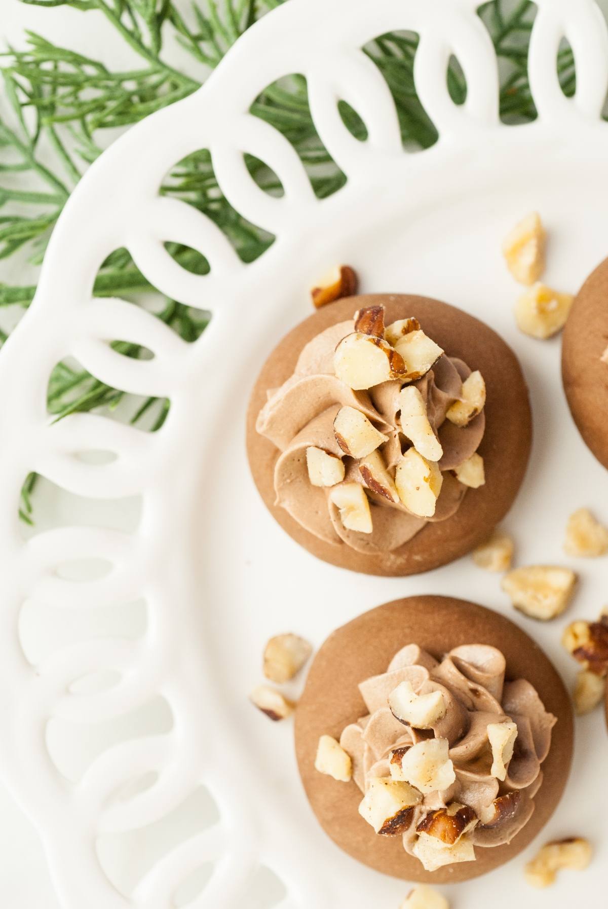 Two Nutellotti - Italian Nutella Cookies with chocolate frosting and chopped nuts rest on a white decorative plate—a delightful treat for those seeking delicious recipes that use Nutella.