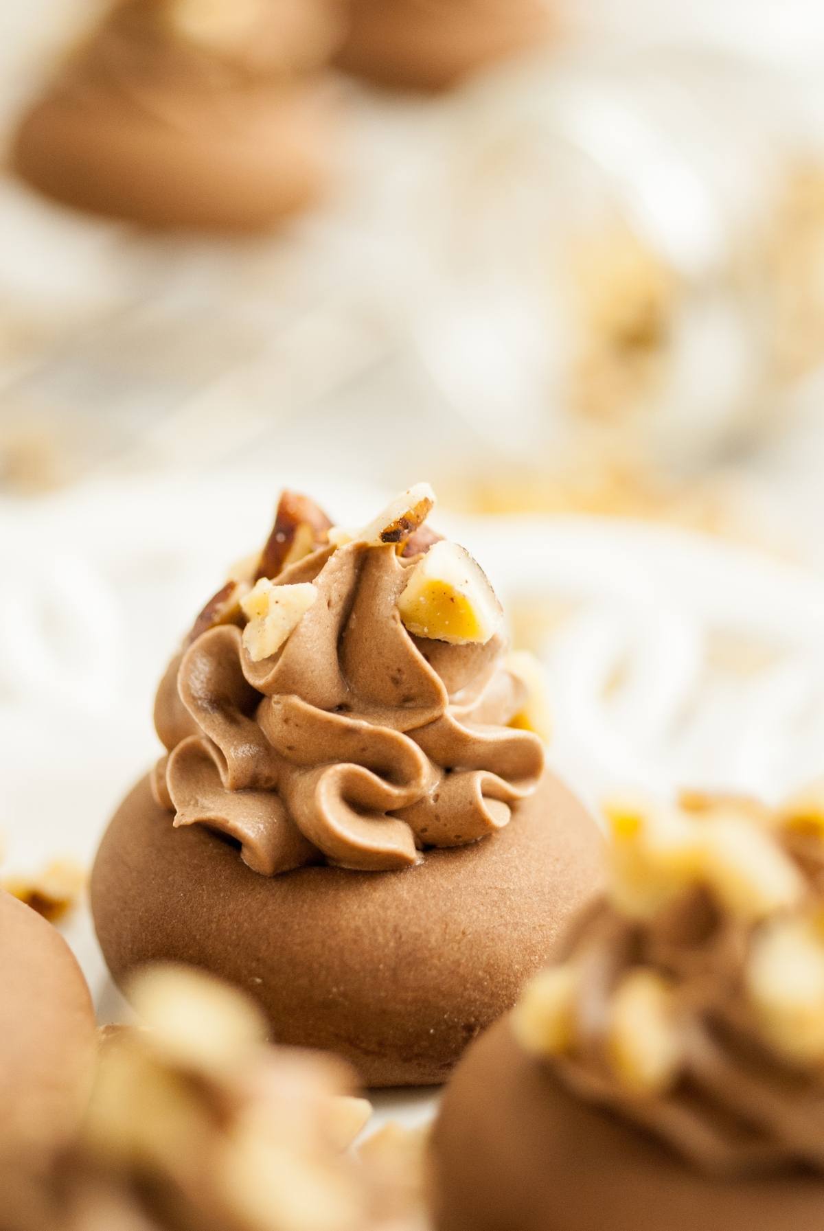 A chocolate cookie topped with swirled chocolate frosting and chopped nuts, inspired by Nutellotti - Italian Nutella Cookies, served on a white plate. Perfect for anyone seeking delicious nutella Christmas cookies.