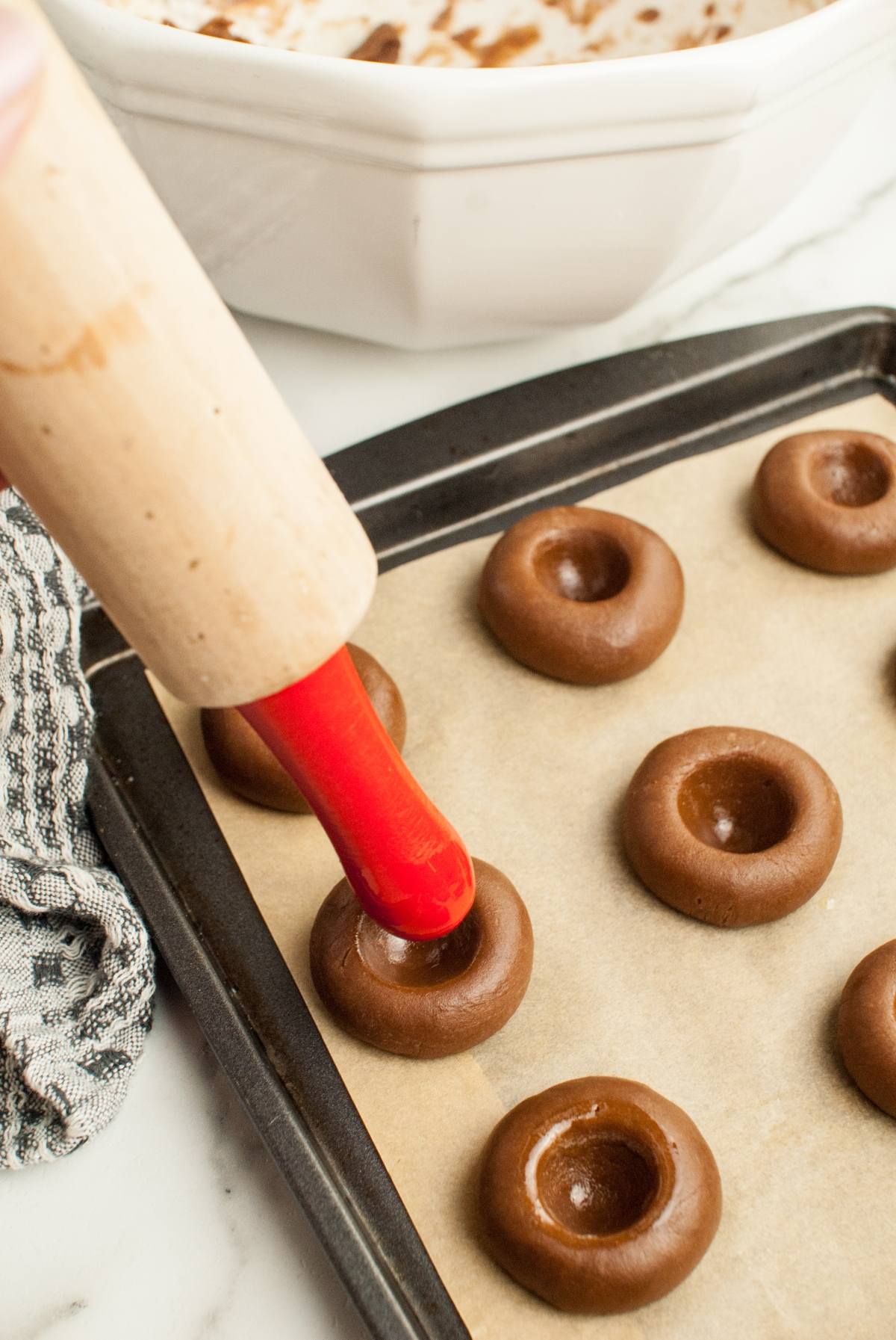 A hand uses a red-handled tool to press indents into chocolate cookie dough for Italian Nutella cookies on a baking sheet.