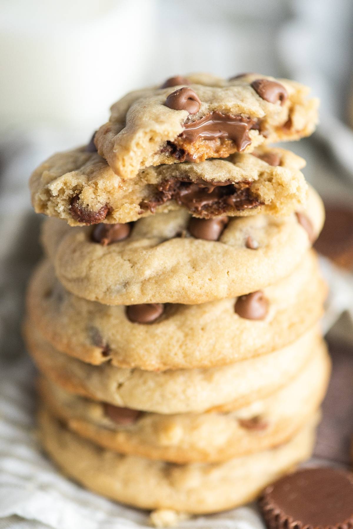 A stack of stuffed chocolate chip cookies, with the top cookie broken to reveal a gooey chocolate center. Made with mini peanut butter cups for an extra indulgent twist.