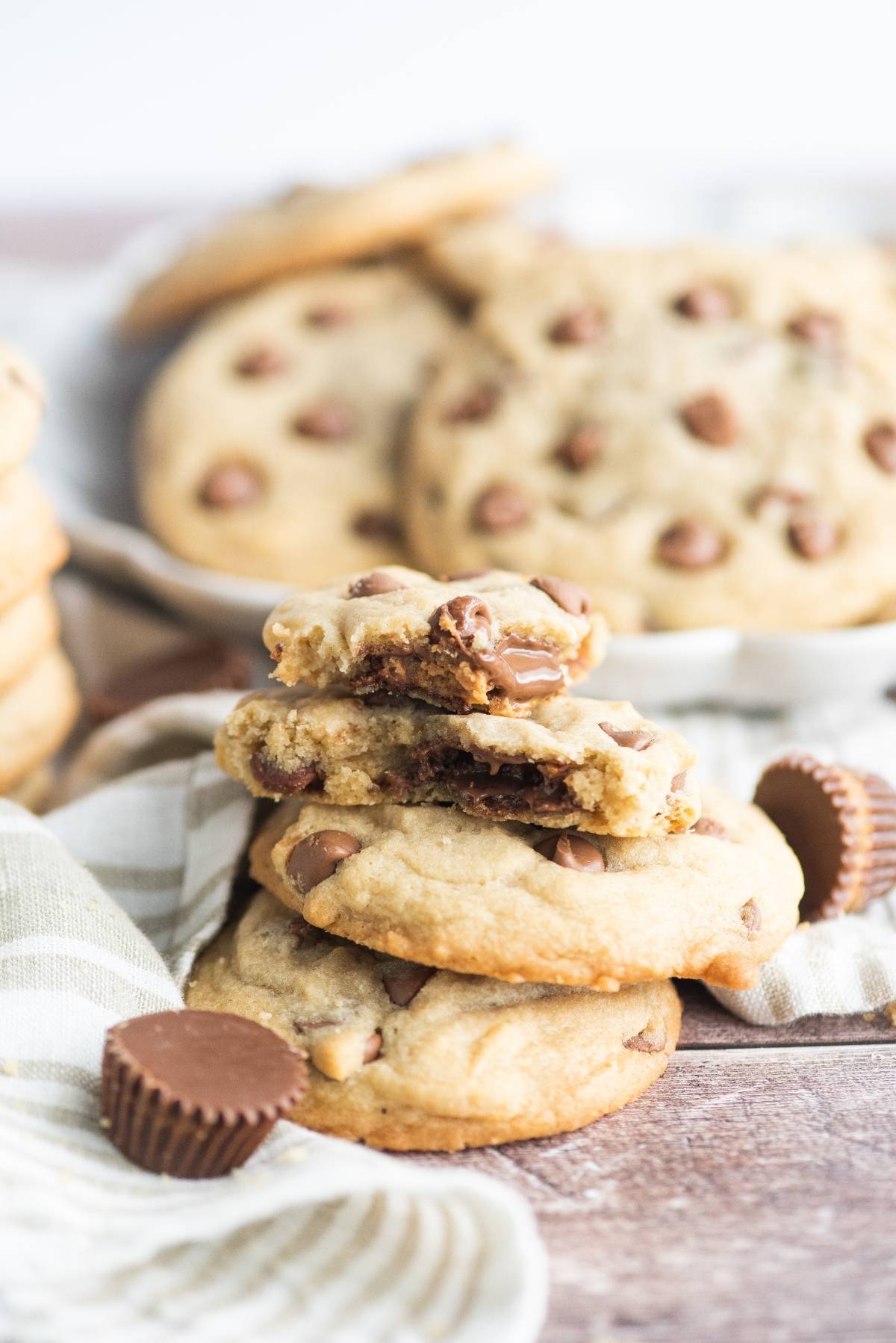 A stack of stuffed chocolate chip cookies, one broken in half, with mini peanut butter cups beside them—perfect for using leftover Halloween treats.