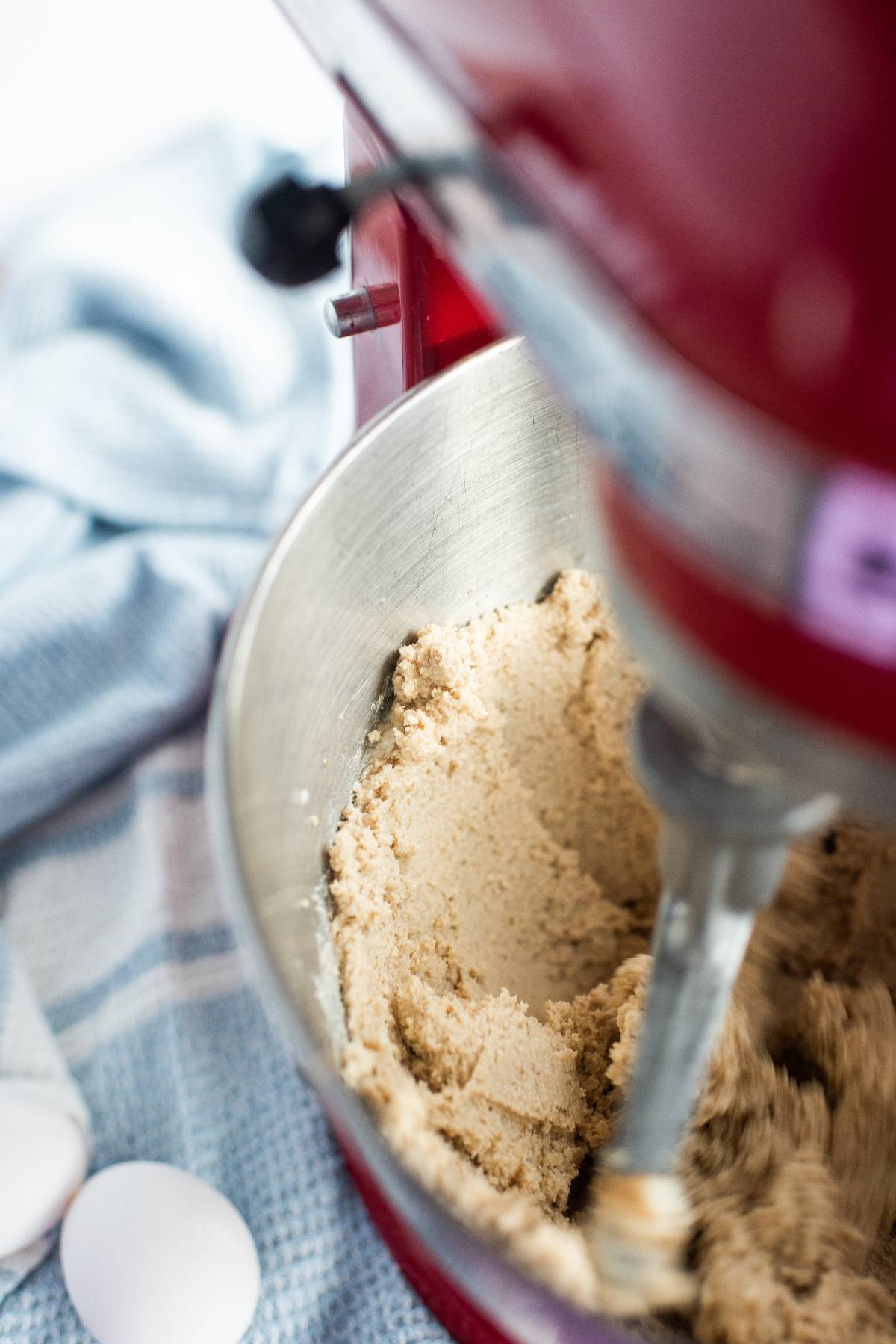 Close-up of peanut butter cup stuffed cookies dough being mixed in a red stand mixer, with eggs and a blue towel nearby.