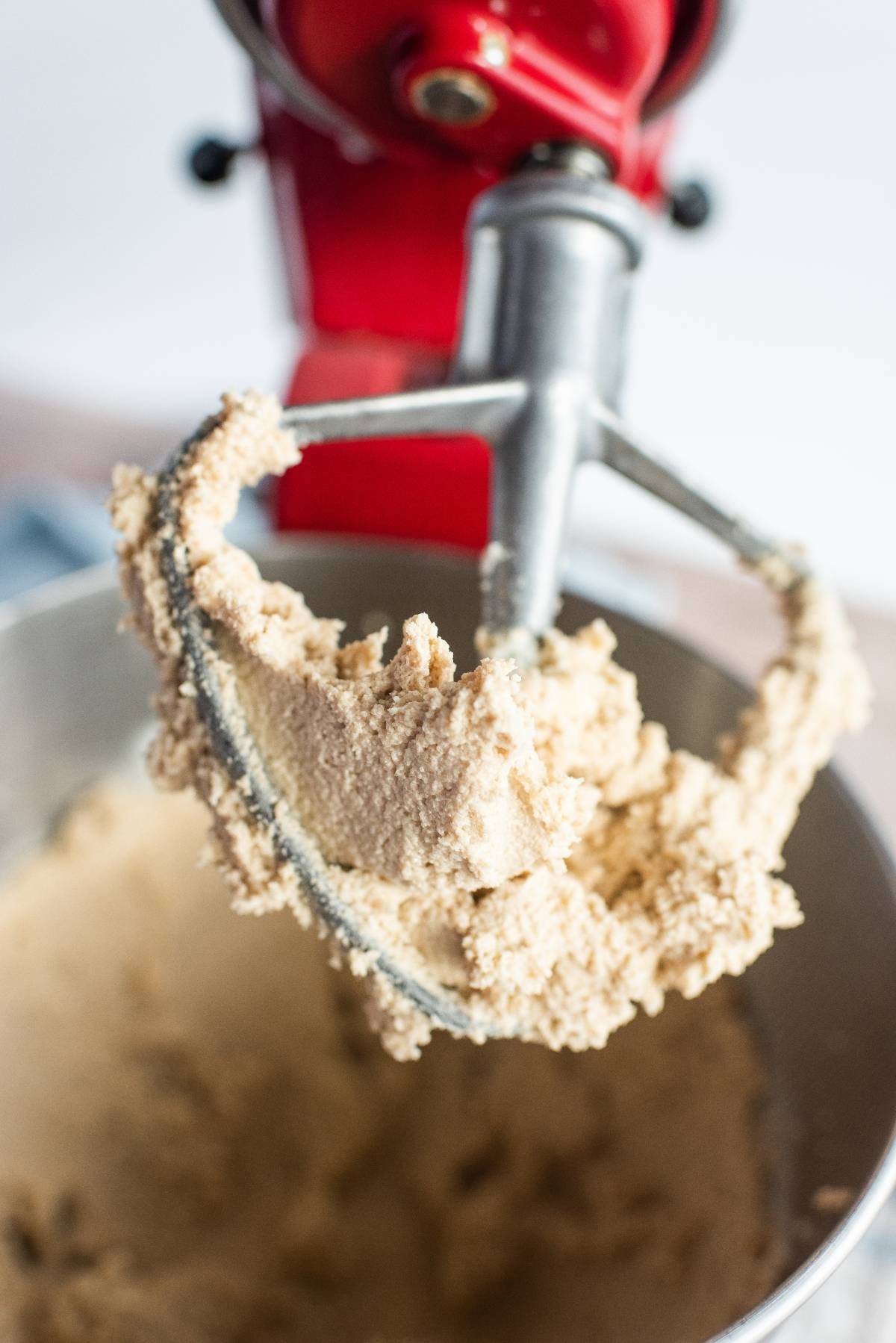 A close-up of a stand mixer paddle with cookie dough attached, above a mixing bowl—perfect for making peanut butter cup stuffed cookies.