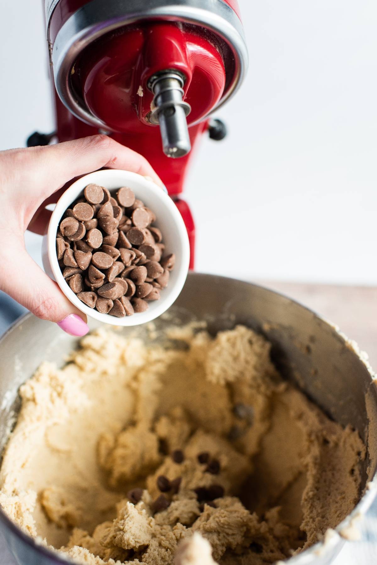 A hand adds chocolate chips to cookie dough in a stand mixer, making peanut butter cup stuffed cookies with mini peanut butter cups—perfect for using leftover Halloween treats.