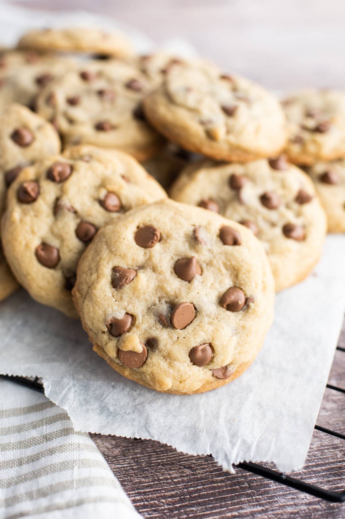 A pile of chocolate chip cookies on parchment paper, with a focus on the cookies in front—these are no ordinary treats, but peanut butter cup stuffed cookies using leftover Halloween treats for an extra delicious surprise.