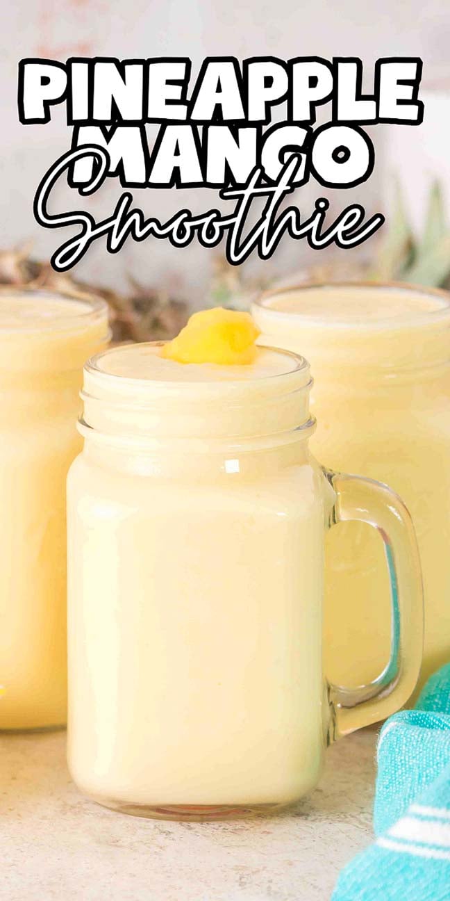 A mason jar filled with a creamy yellow Pineapple Mango Smoothie, topped with fruit, sits beside a blue towel.