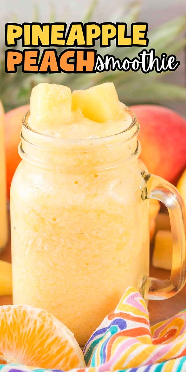 A mason jar filled with Pineapple Peach Smoothie, topped with pineapple chunks, sits beside fresh fruit and a colorful napkin.