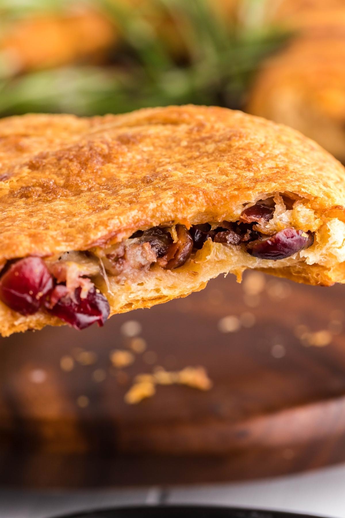 Closeup of a golden, flaky pastry with a filling of cranberries and nuts, held up to show the inside—just like a tempting crescent wreath appetizer.