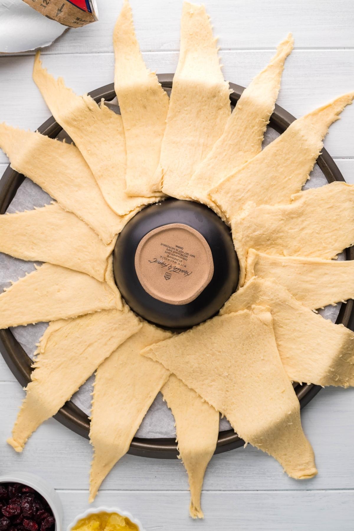 A baking tray with crescent dough triangles arranged in a sunburst around an upside-down bowl, ready to create a stunning crescent wreath appetizer.