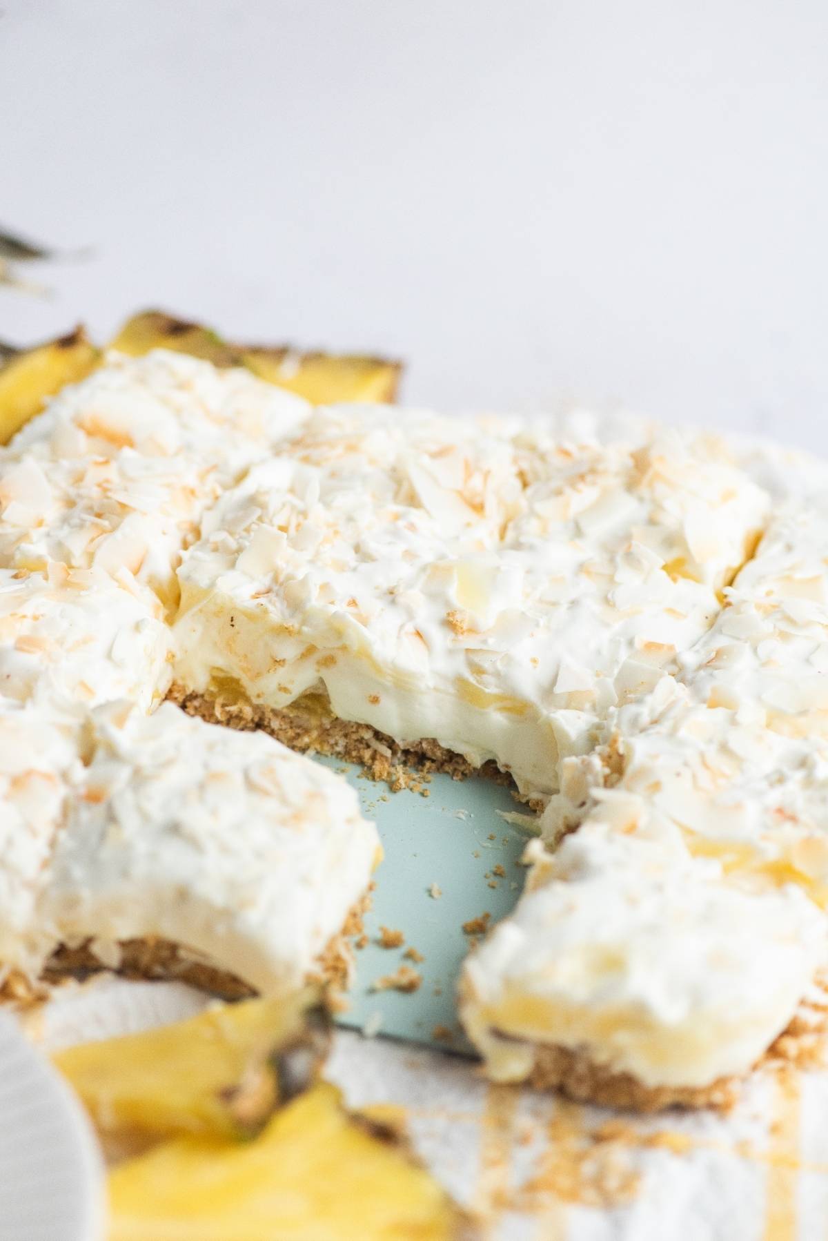 A creamy pie with a crumbly crust, topped with toasted coconut and a hint of pineapple lush—perfect as a dessert for a summer BBQ, with a slice already removed to tempt your guests.