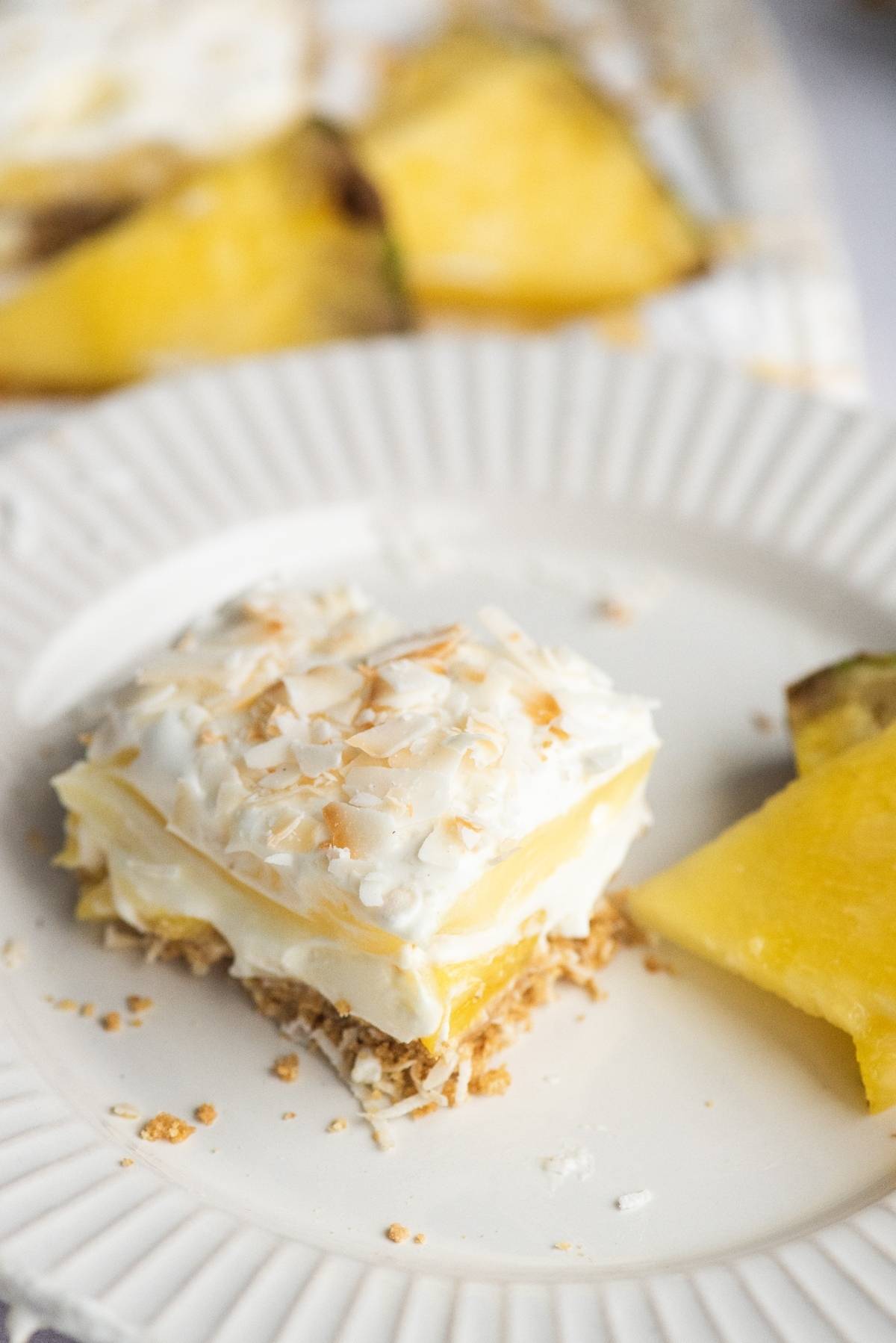 A slice of creamy summer dessert, this Hawaiian pineapple and coconut cake is topped with whipped topping and toasted coconut, served on a white plate.