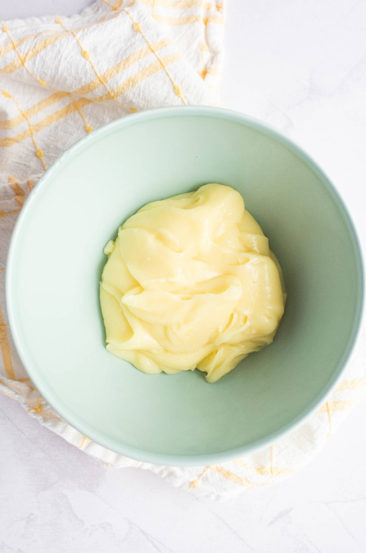A bowl of creamy yellow custard sits on a striped kitchen towel, making a perfect dessert for a summer BBQ.
