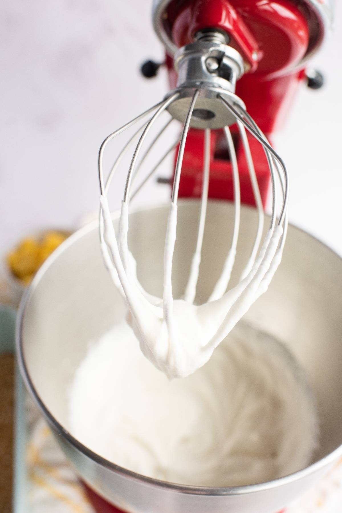 A stand mixer with whipped cream on the whisk attachment above a bowl of more whipped cream—perfect for topping a creamy summer dessert or your favorite no bake cake recipe.